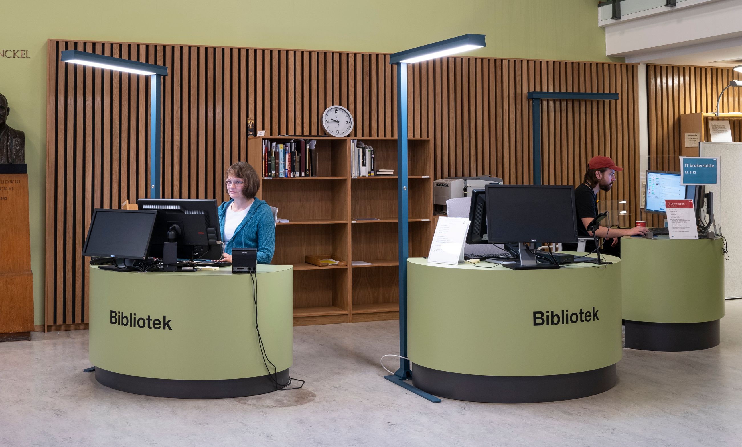 en dame sitter ved en grønn skranke i et bibliotek