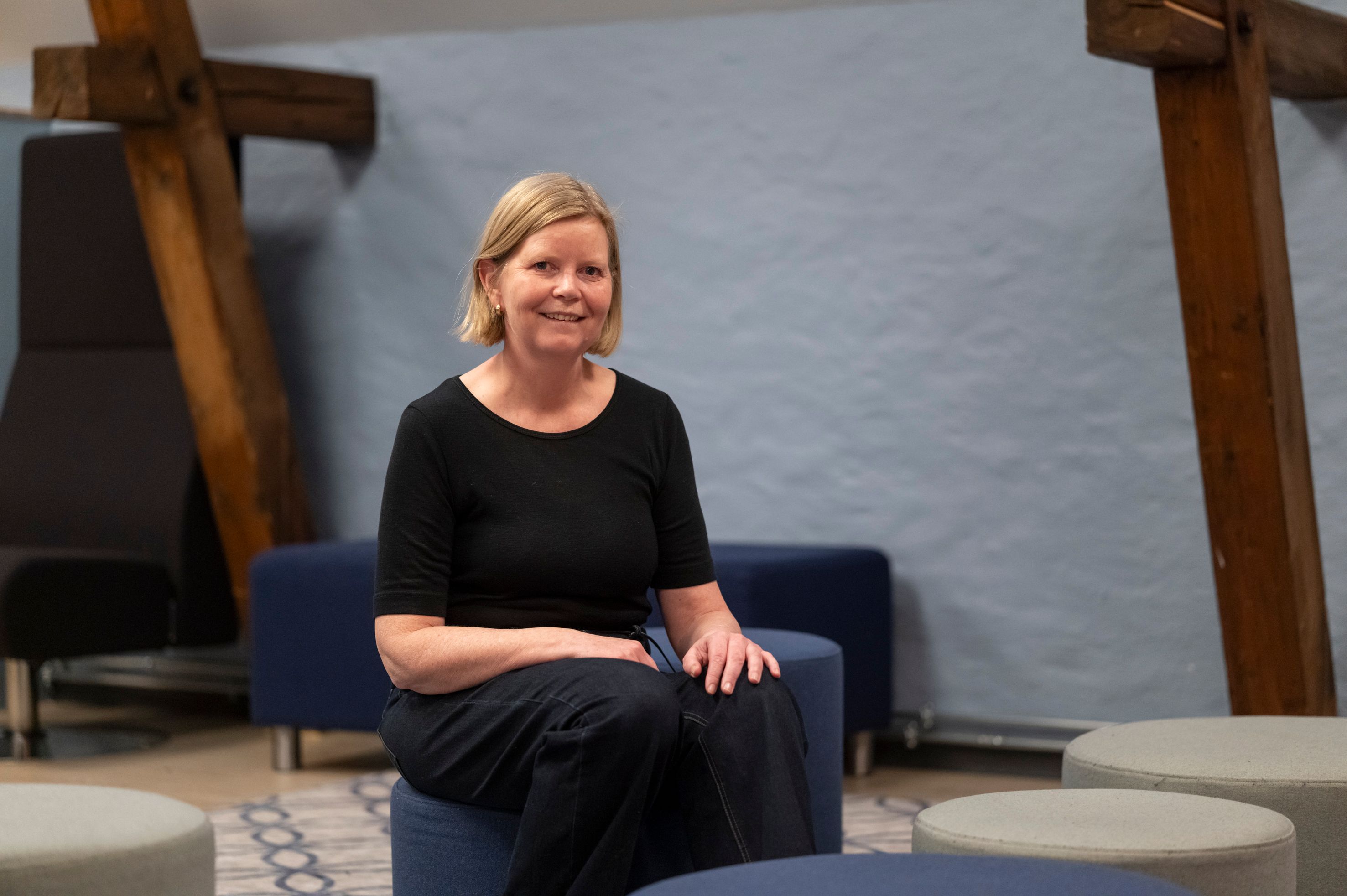 Smiling blonde woman sitting on a blue ottoman.