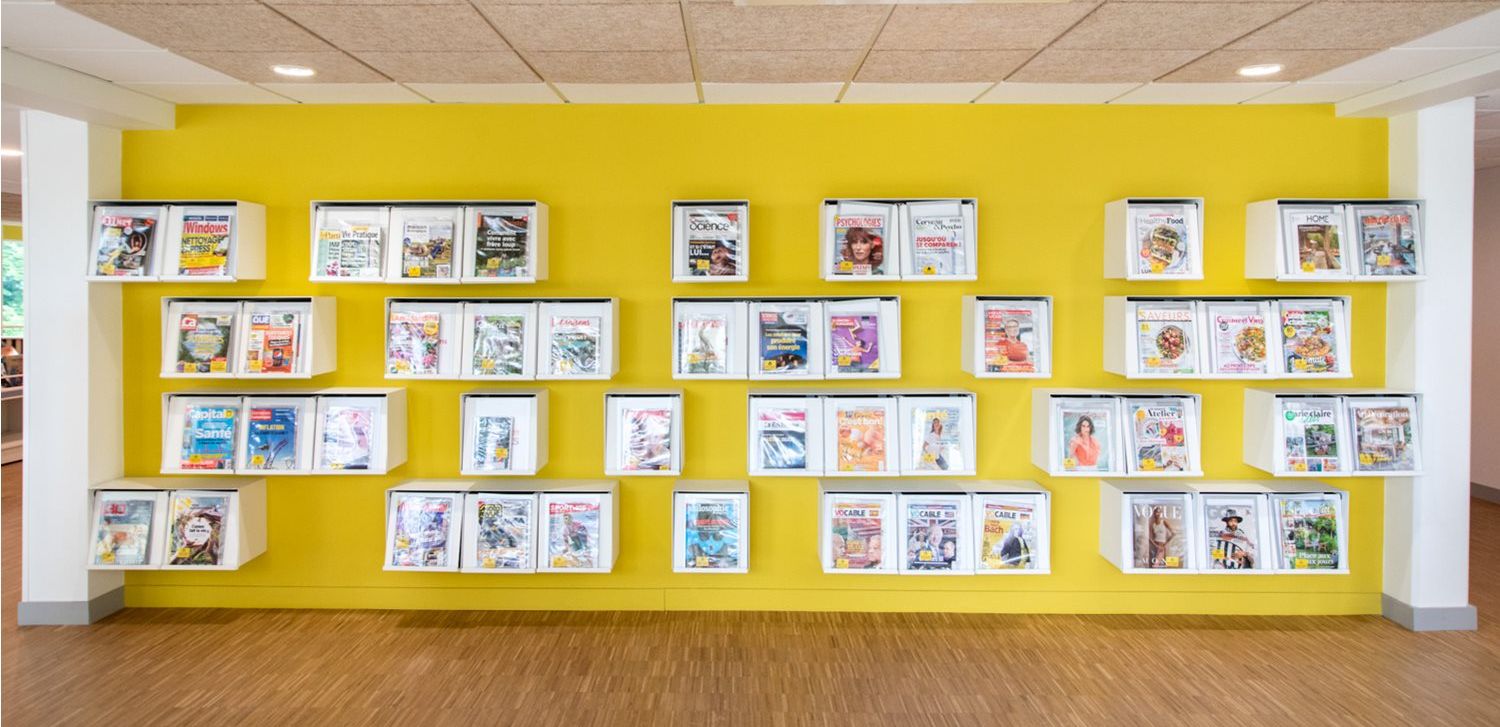 en gul vegg på biblioteket med hvite bokser for tidsskrifter