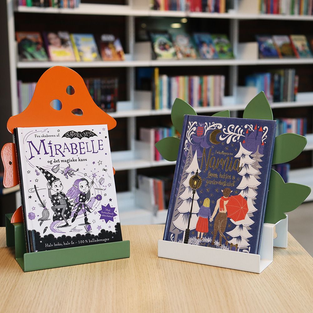 Children's books "Mirabelle" and "Narnia" displayed in mushroom and leaf-shaped stands on a wooden table.