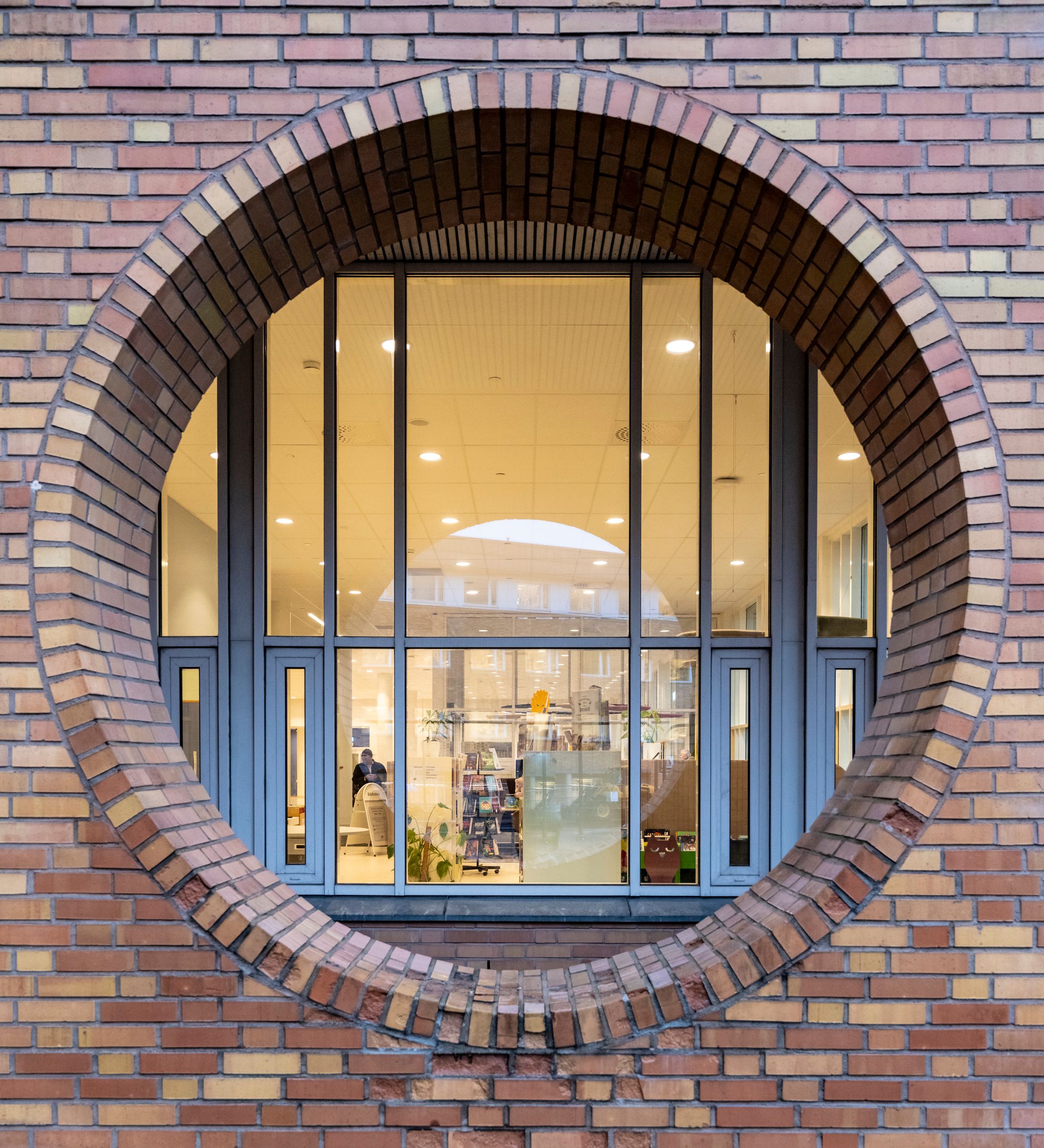 A large circular window framed by brick, revealing a brightly lit interior.