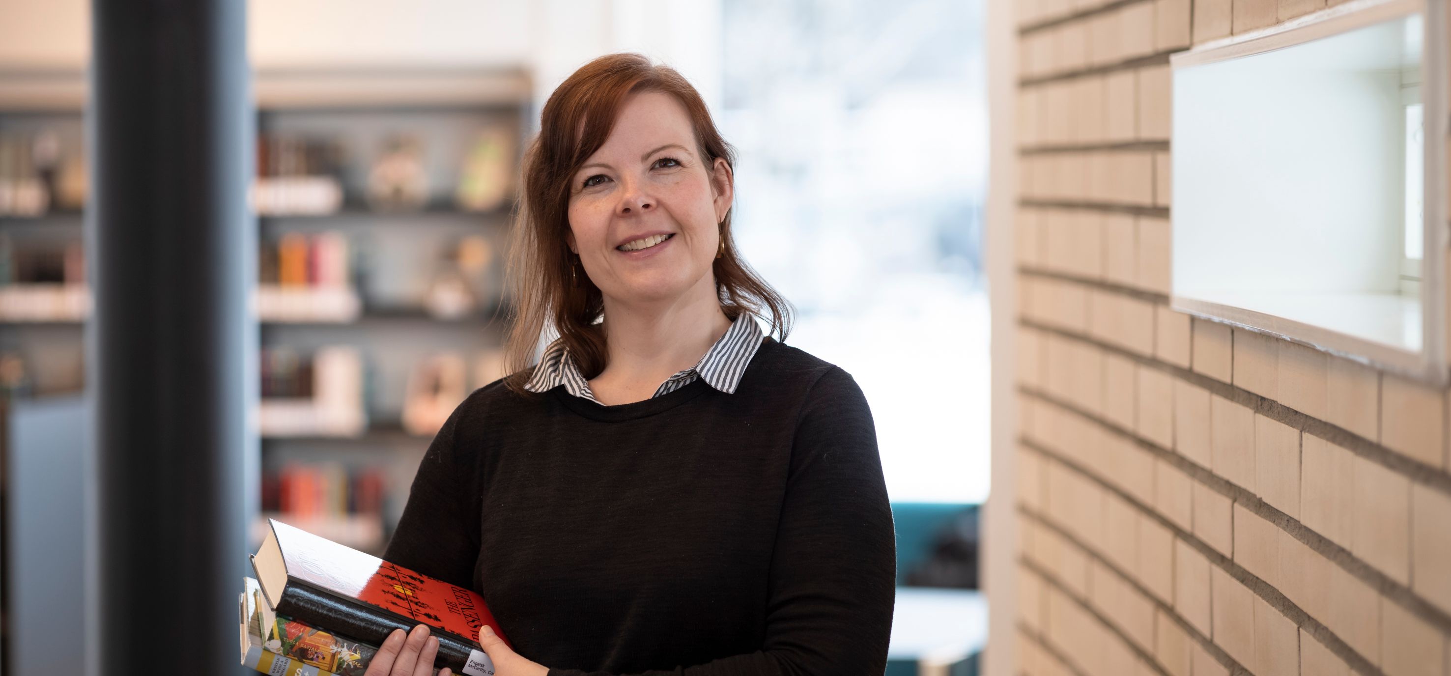 en kvinne holder en bok i hendene sine i et bibliotek.