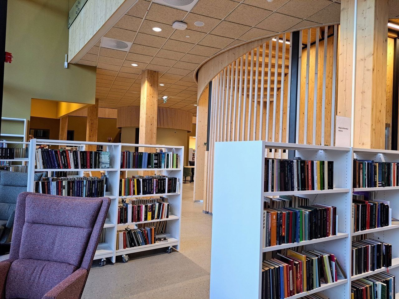 A modern library interior with white bookshelves, a purple armchair, and wooden architectural details.