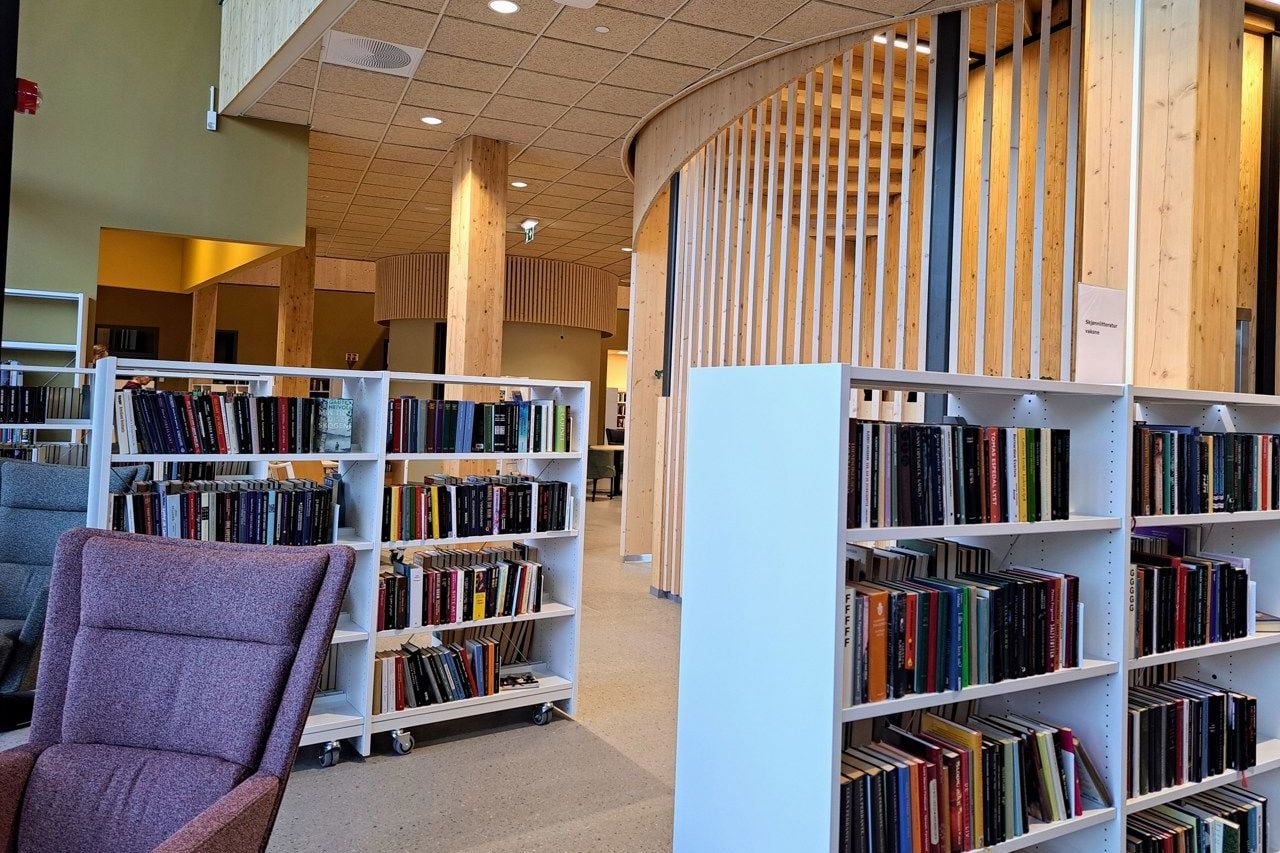 A modern library interior with white bookshelves, a purple armchair, and wooden architectural details.