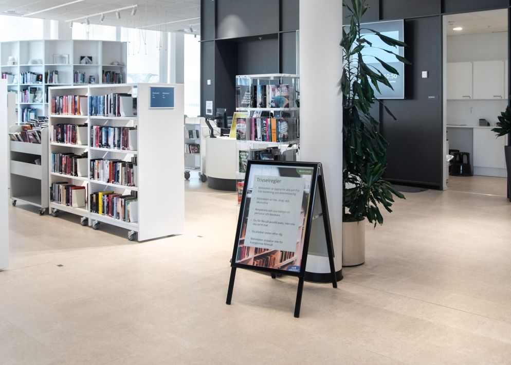 et bibliotek med mange bøker på hyllene og et skilt på gulvet.