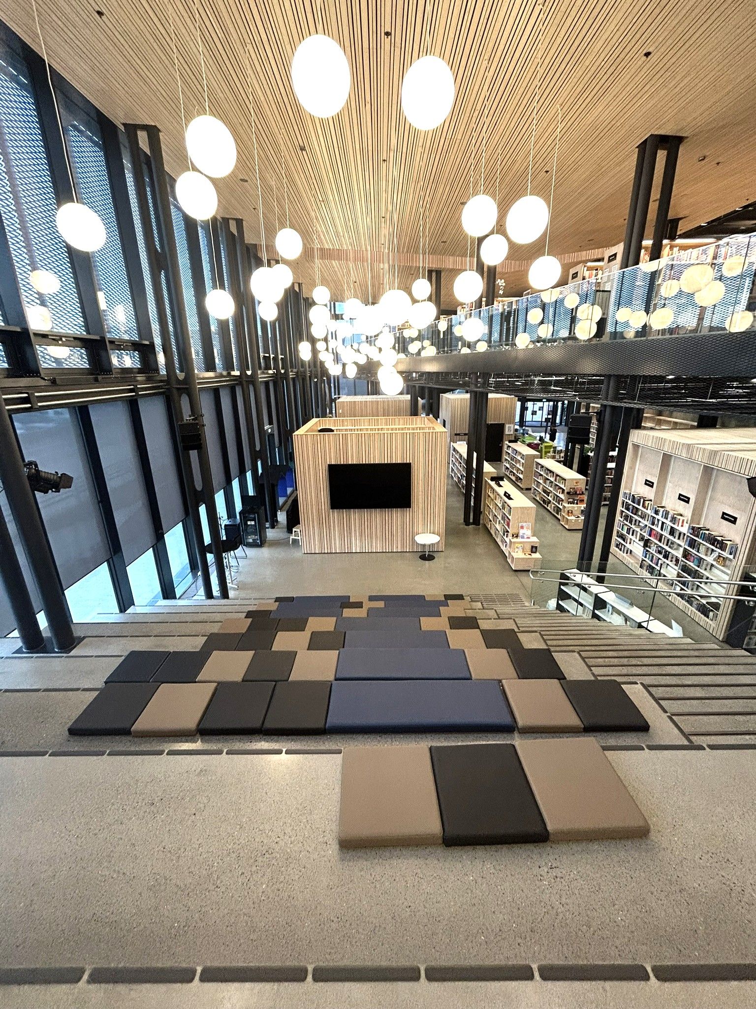 A large, modern library interior with tiered seating, suspended globe lights, and bookshelves on multiple levels.