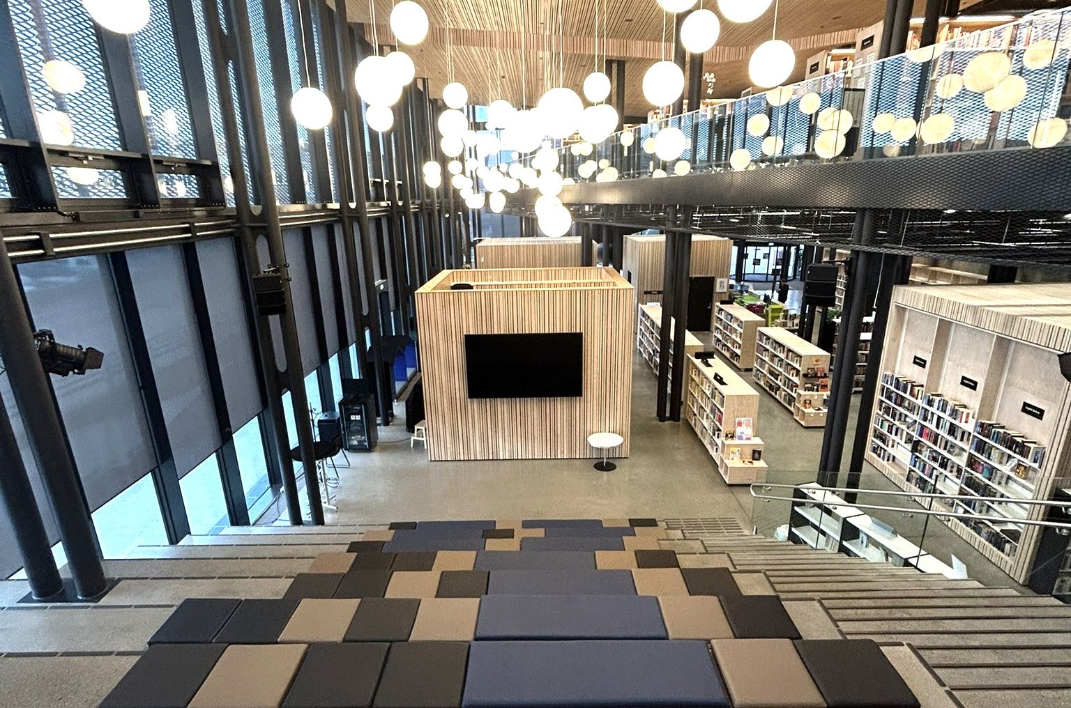A large, modern library interior with tiered seating, suspended globe lights, and bookshelves on multiple levels.