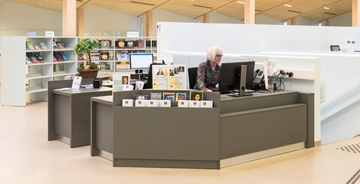 en dame sitter ved en grå bibliotekskranke i et moderne bibliotek med tretak