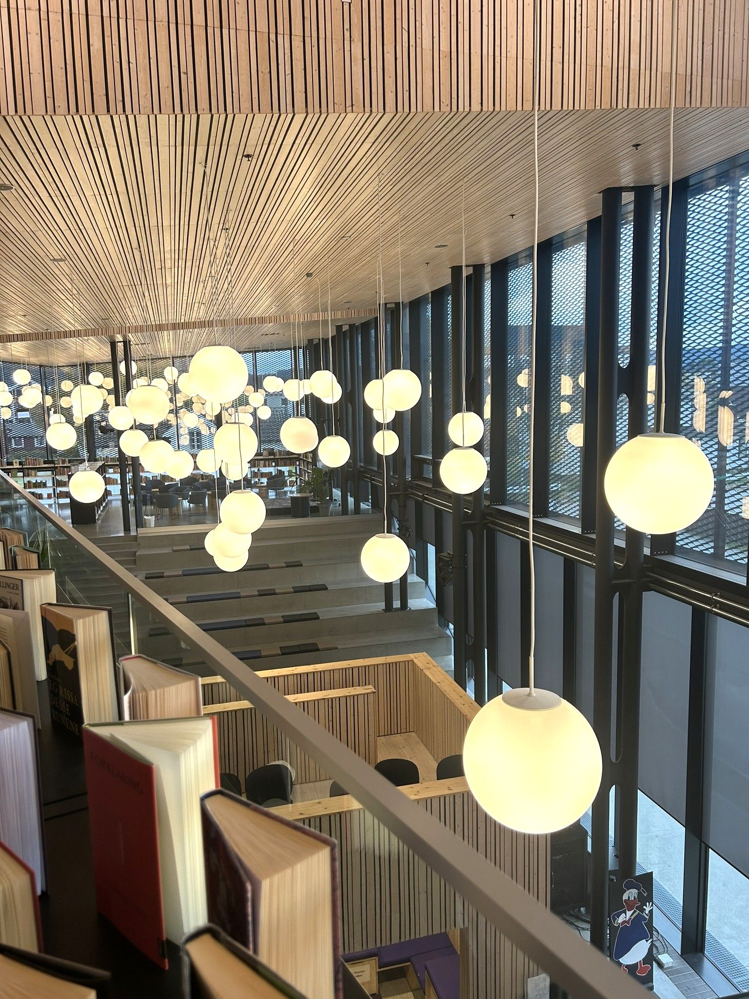 Modern library interior with dozens of glowing spherical pendant lights, tiered seating, and books lining a glass railing.