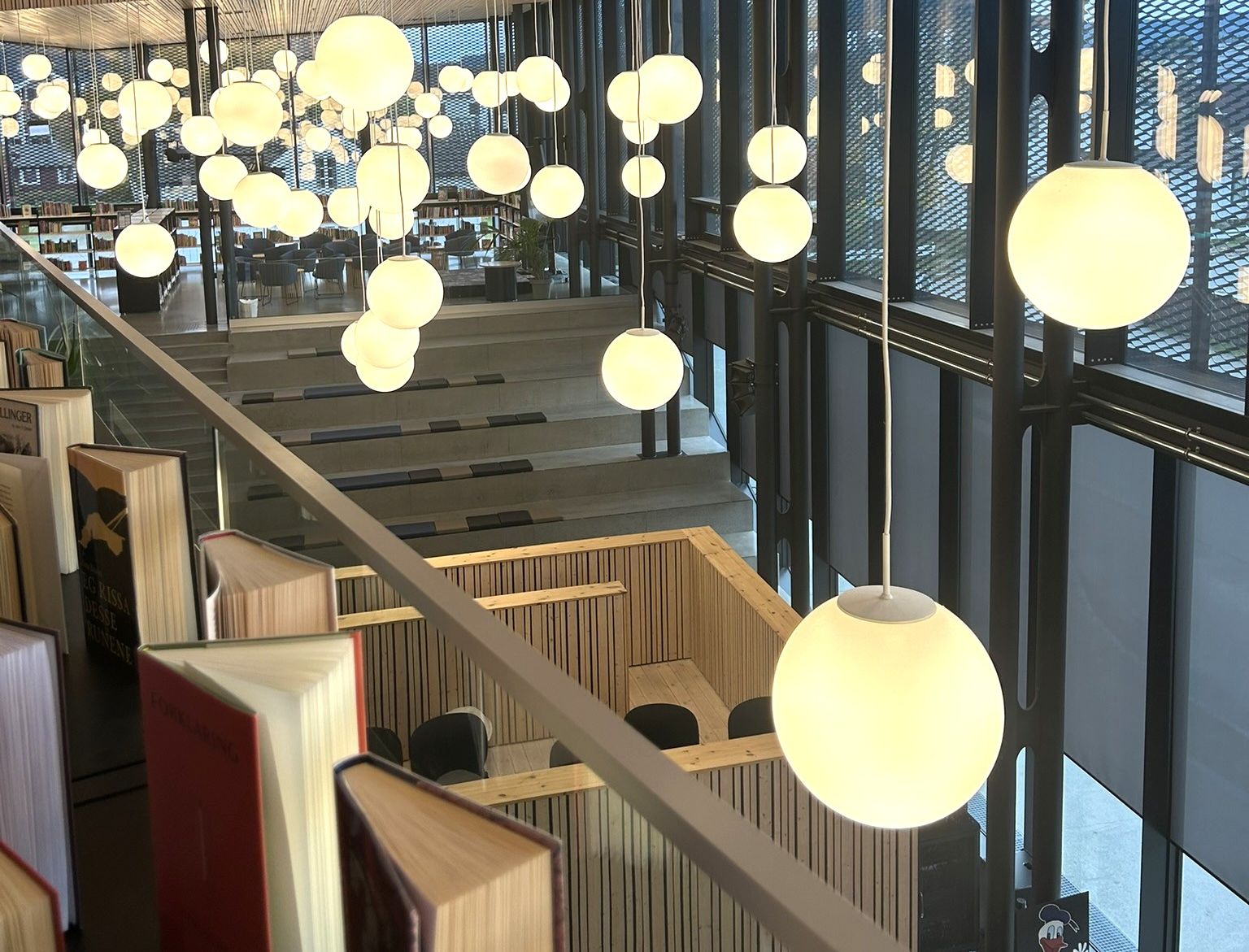 Modern library interior with dozens of glowing spherical pendant lights, tiered seating, and books lining a glass railing.