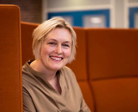 biblioteksjefen i prosgrunn sitter på en sofa og smiler til kameraet.