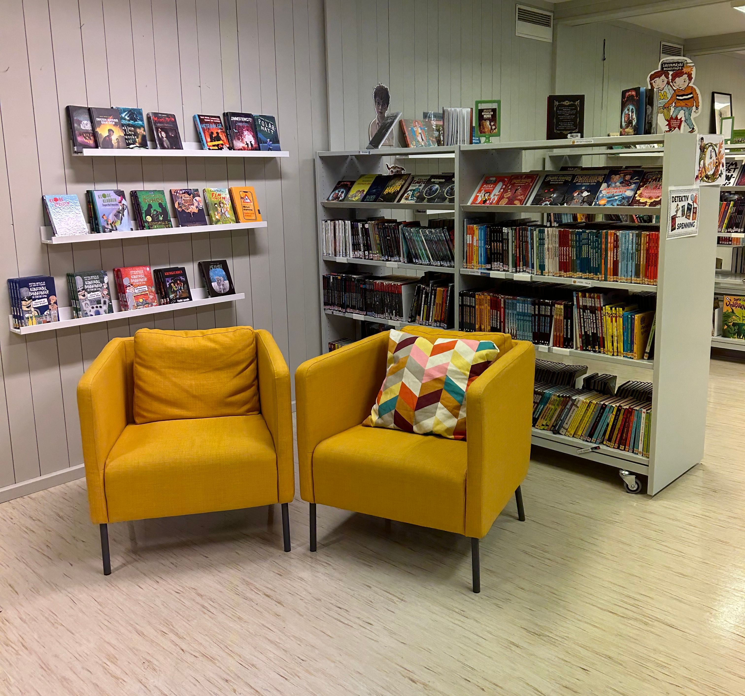 two yellow chairs in a library with books on shelves including one titled ' a christmas carol '