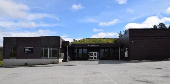 A modern dark building named Rindalshuset with a green grass roof.