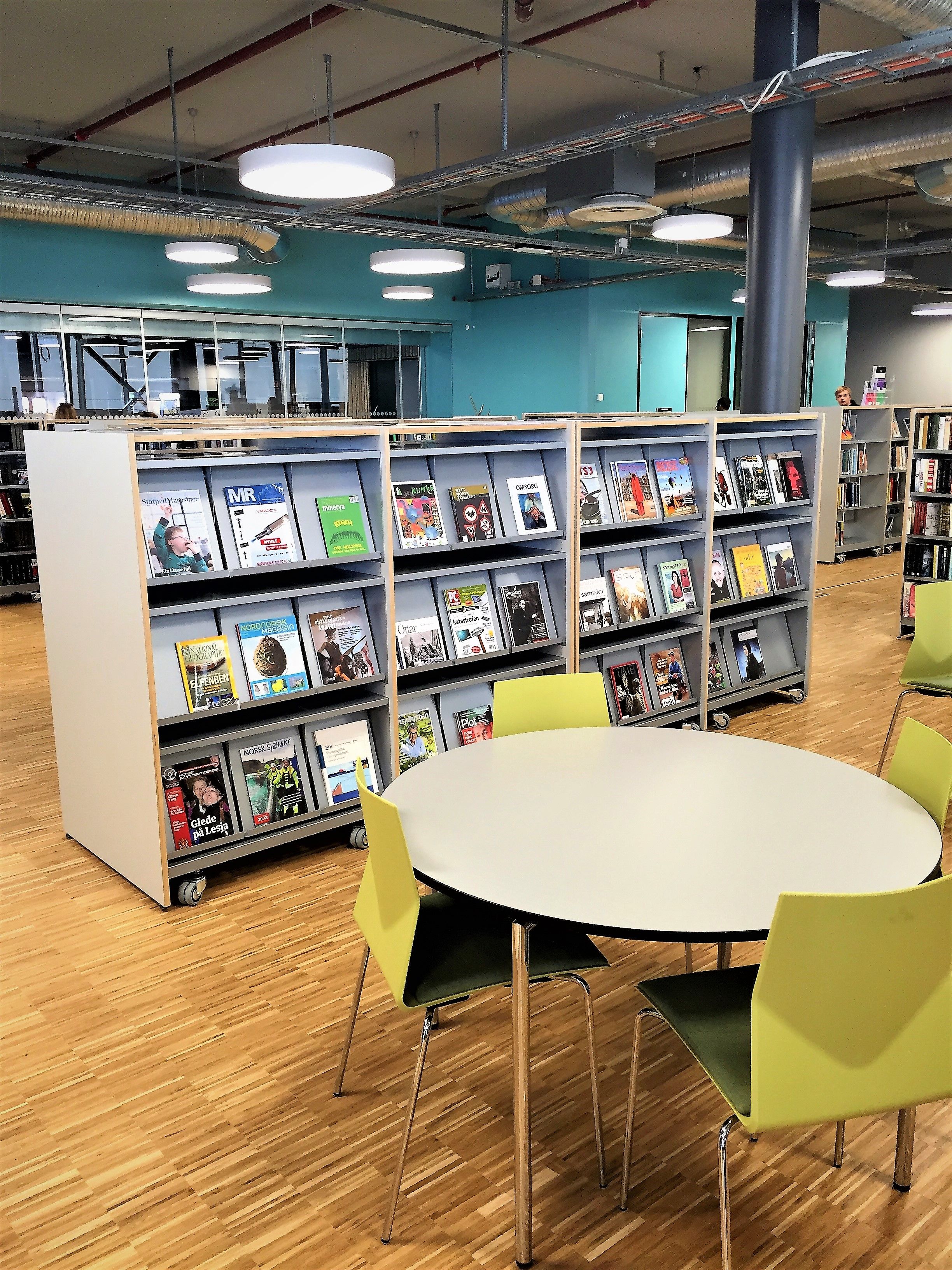 et bord og stoler i et bibliotek med magasiner på hyllene, inkludert en som sier mr