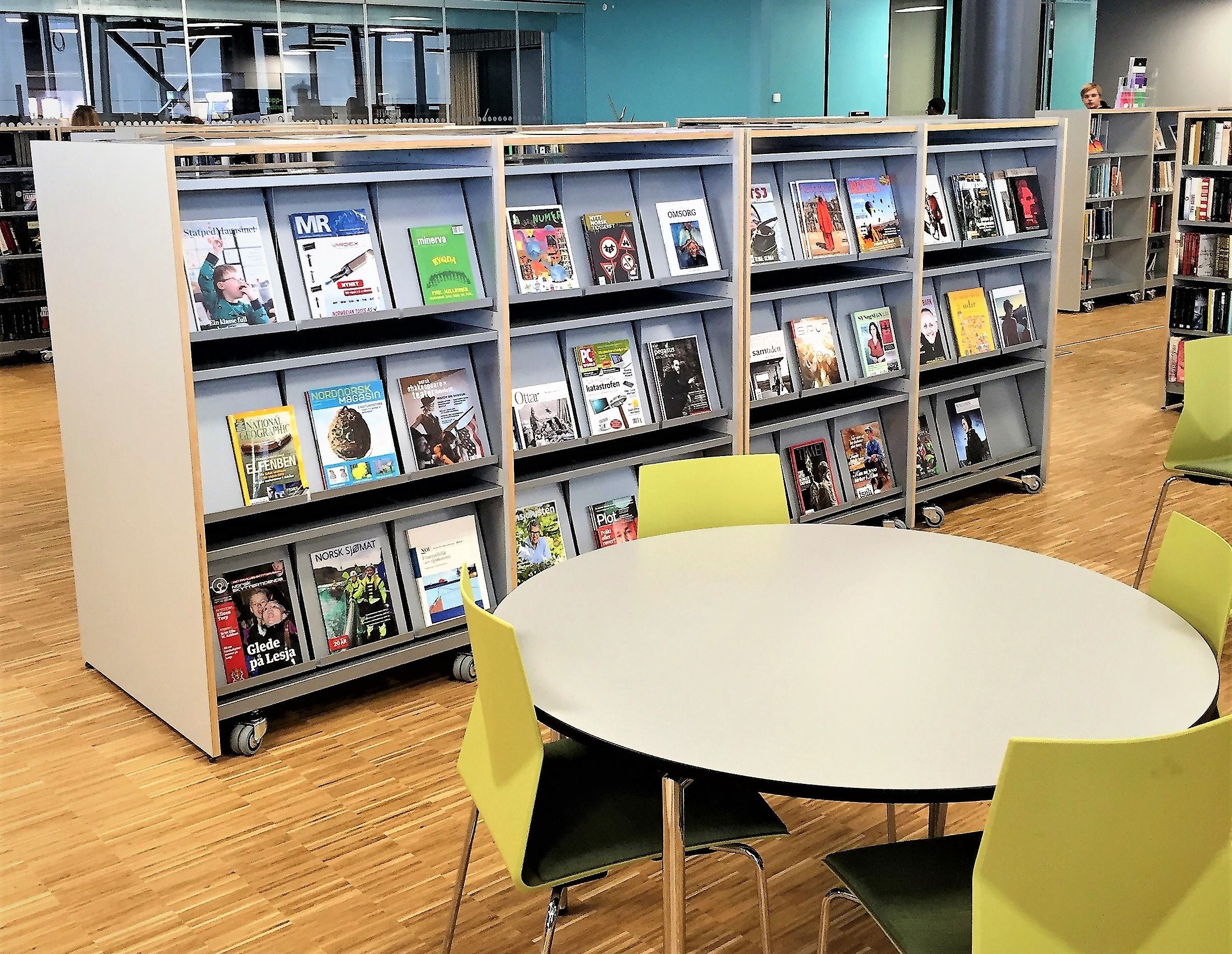 et bord og stoler i et bibliotek med magasiner på hyllene, inkludert en som sier mr