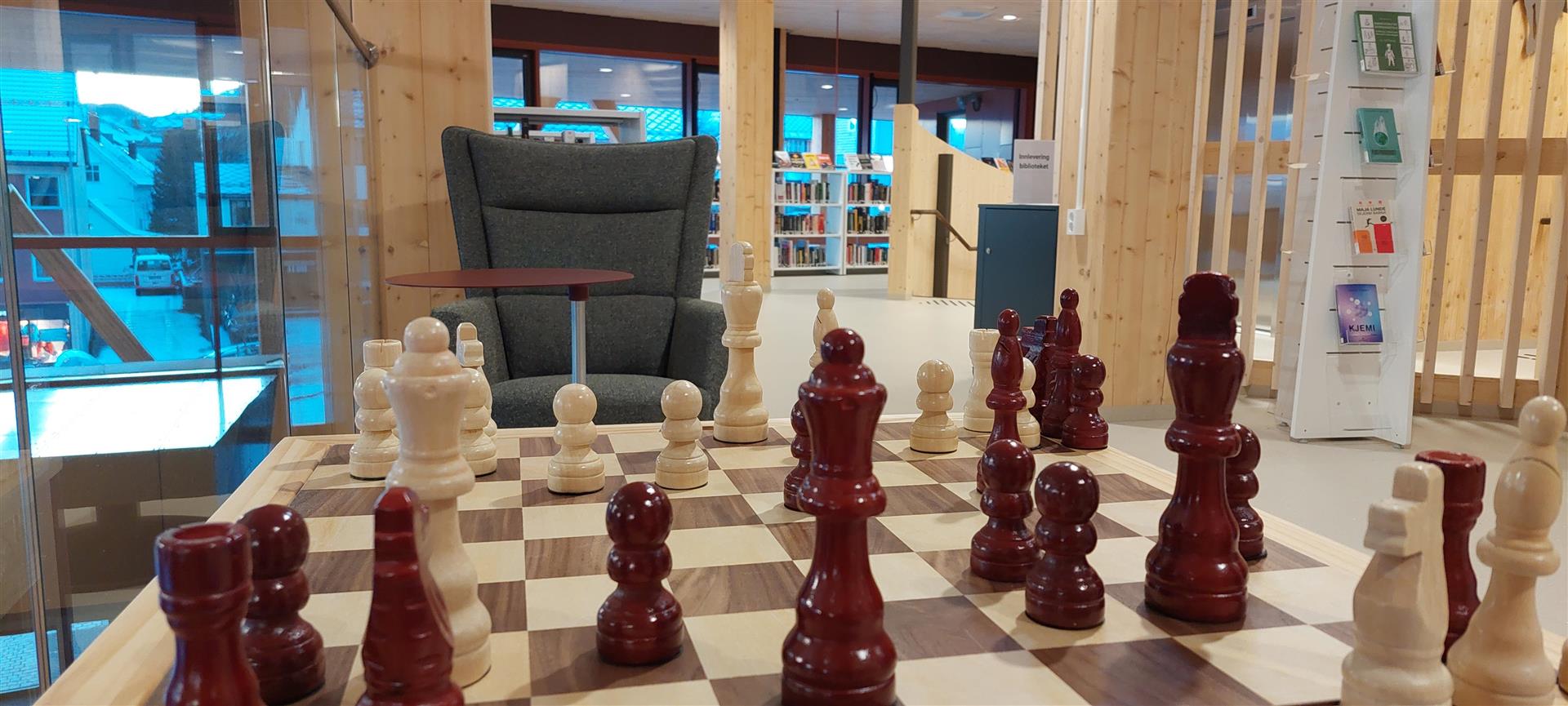Large wooden chess set with dark red and light pieces in a modern library.