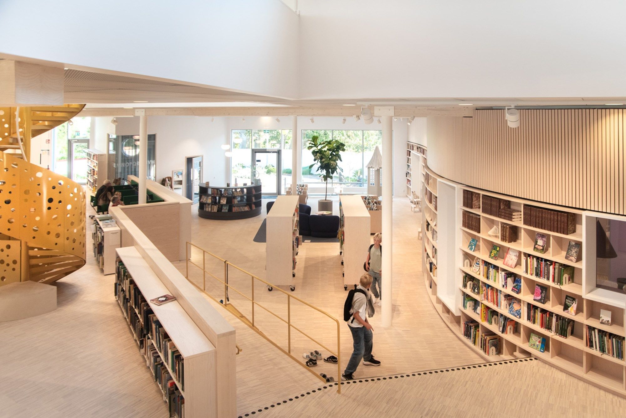 et oversiktsbilde for et bibliotek med naturfargede reoler og en gul trapp