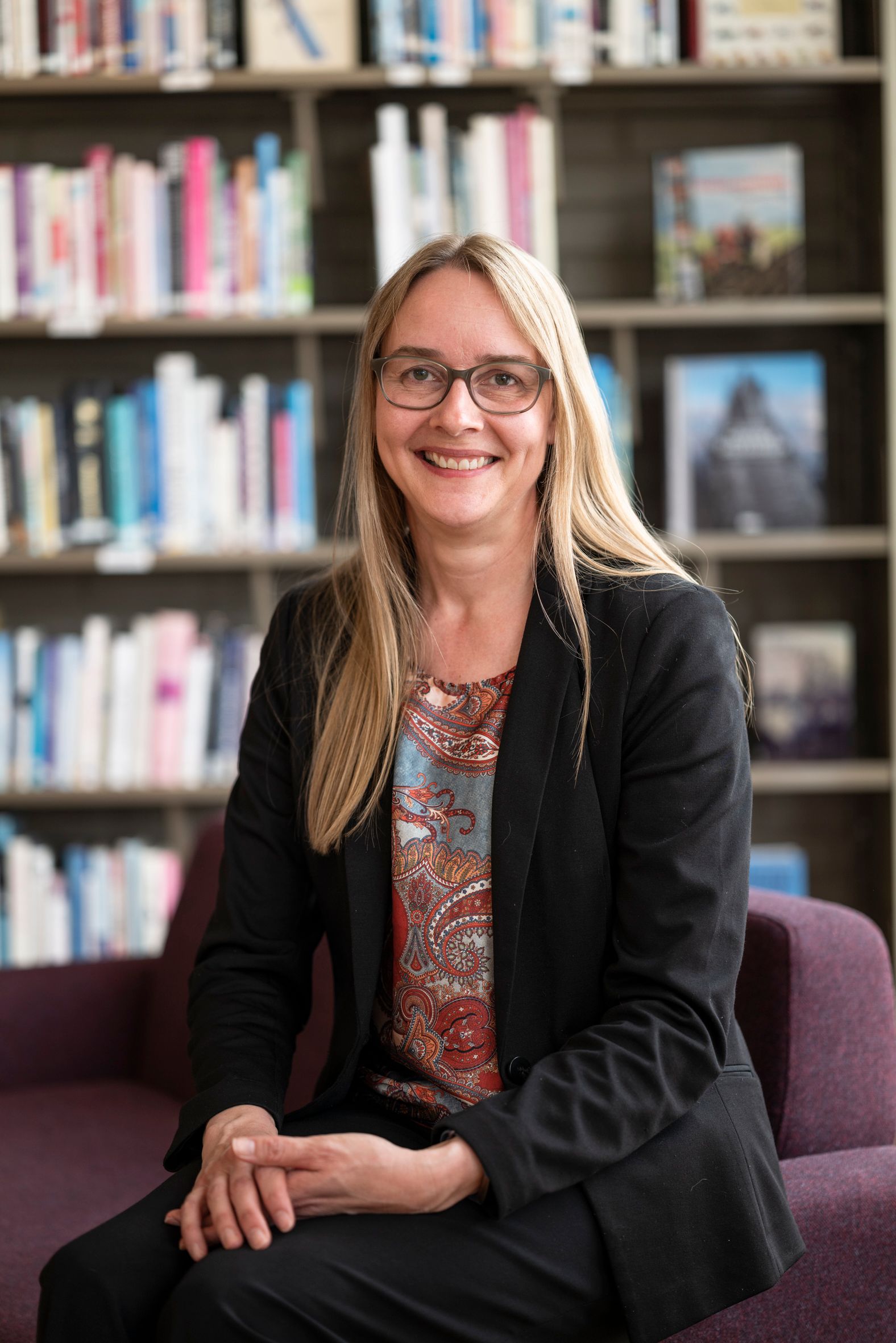 biblioteksjefen i Tynset sitter foran en bokhylle på et bibliotek.