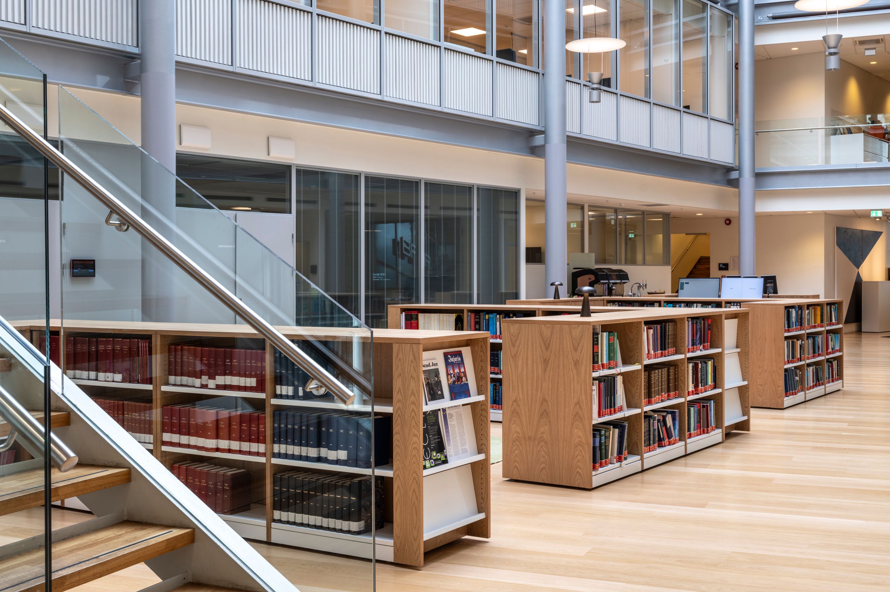 Bright, modern library interior with rows of wooden bookshelves and a glass staircase.