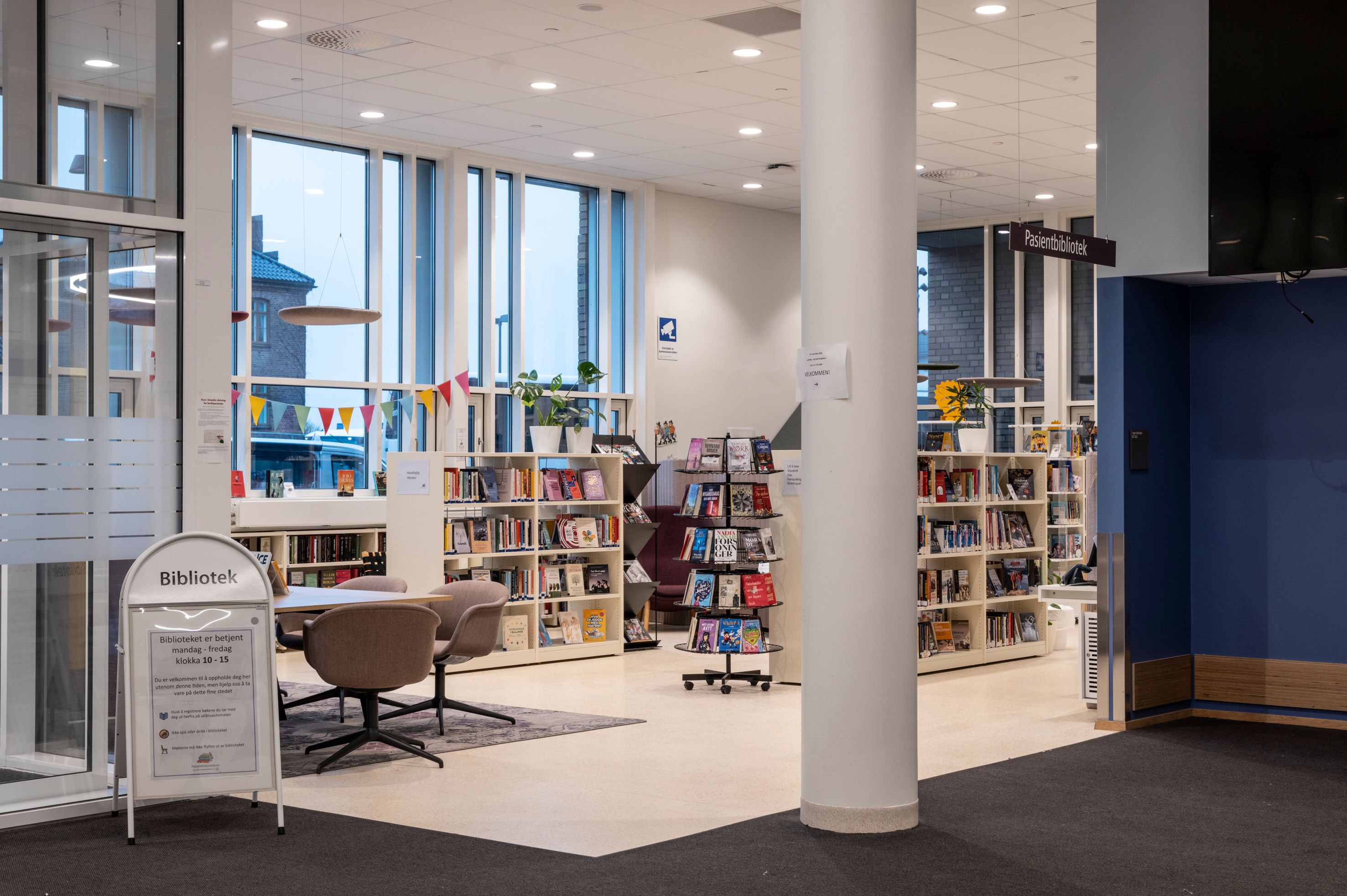 Bright library interior with bookshelves, a small seating area, and large windows.