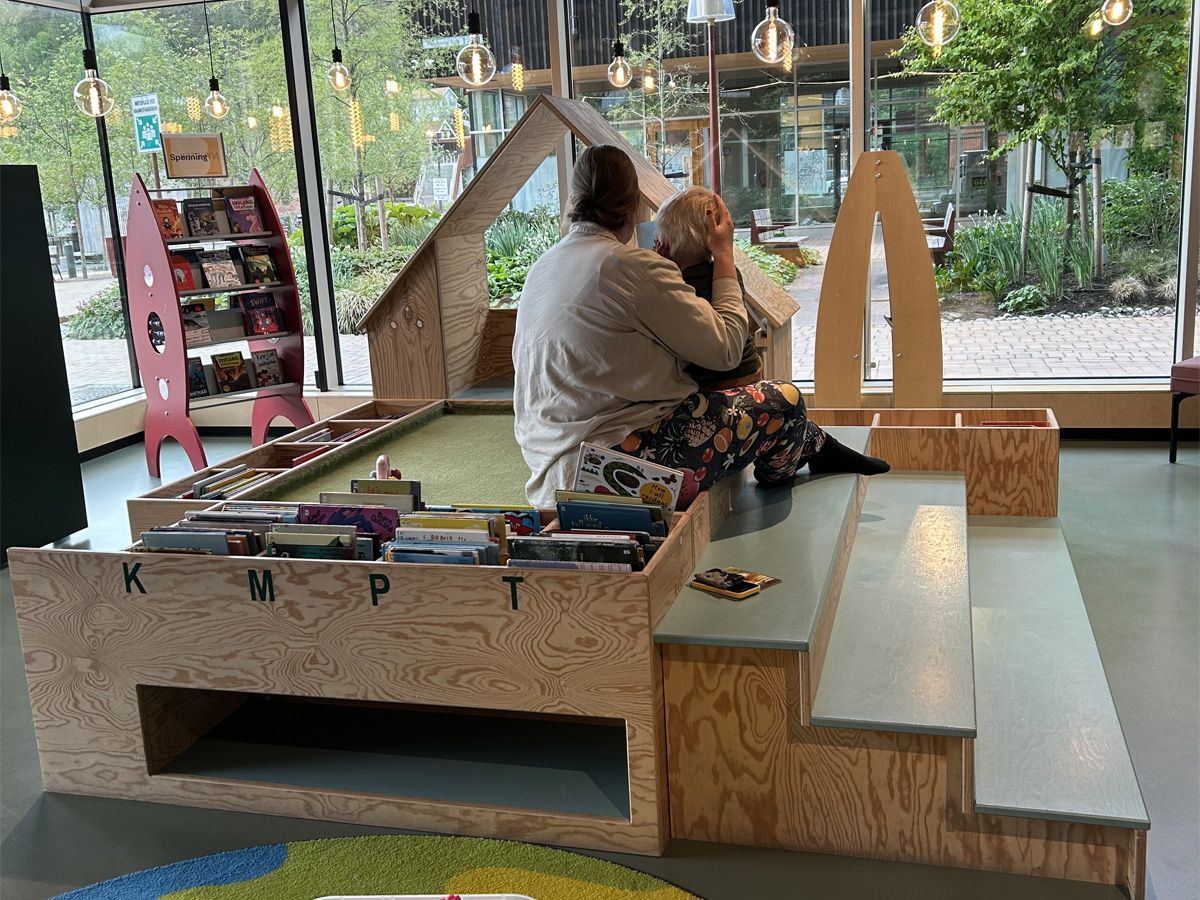 en dame og et barn sitter på et podium i et bibliotek