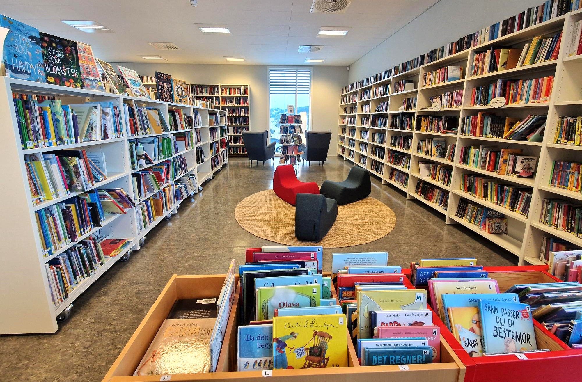A bright, modern library with many bookshelves, colorful contemporary seating, and book display bins.