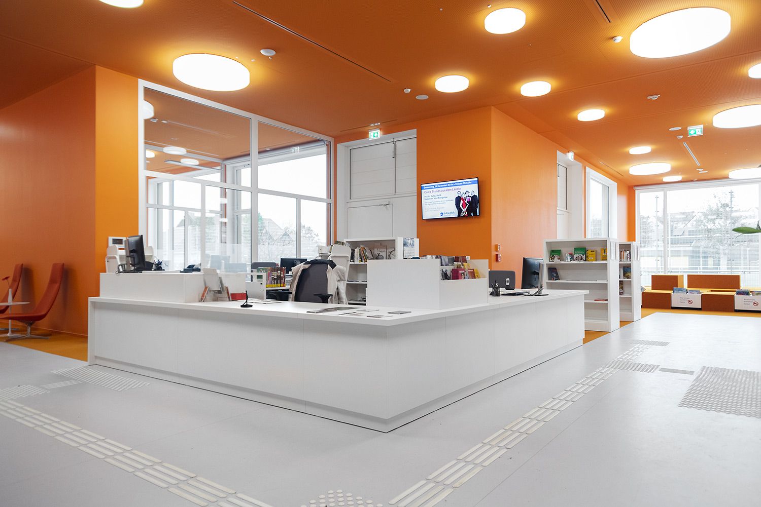 a reception desk in a library with orange walls and white floors .