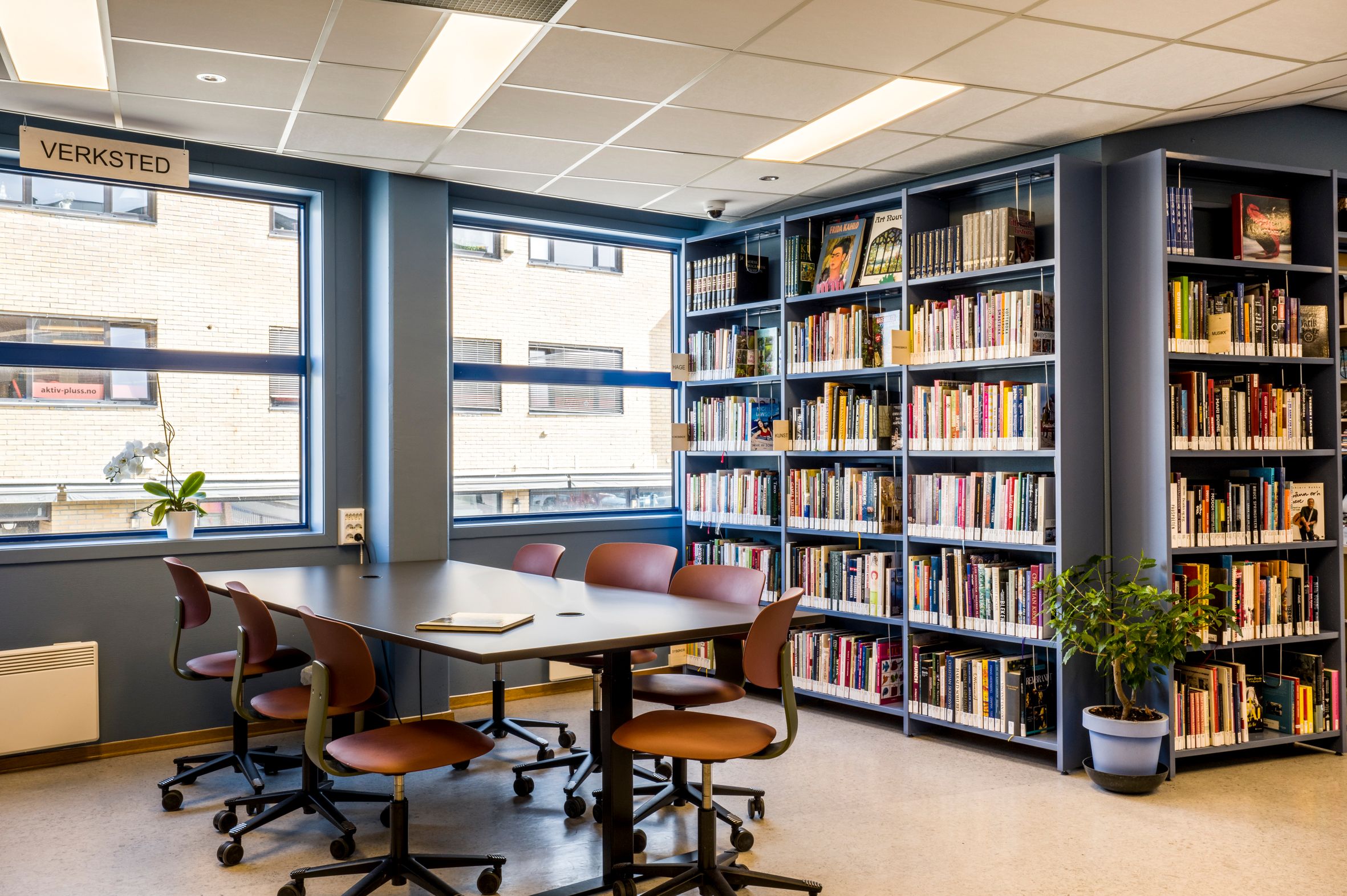 et bibliotek med høye bokreoler og et stort bord med mange stoler rundt