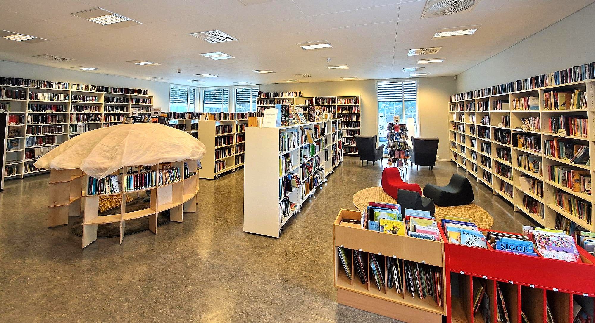 A brightly lit modern library with numerous bookshelves, comfortable seating areas, and a unique mushroom-shaped display.