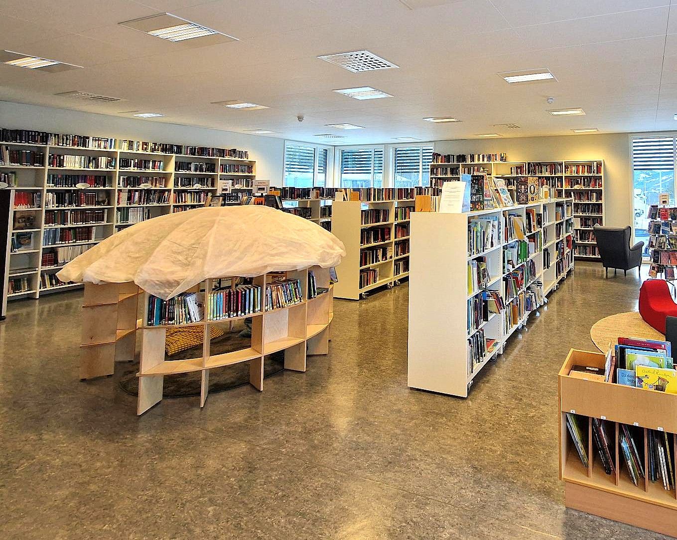 Interior view of a modern library with rows of bookshelves, a unique mushroom-shaped reading nook, and comfortable seating areas.