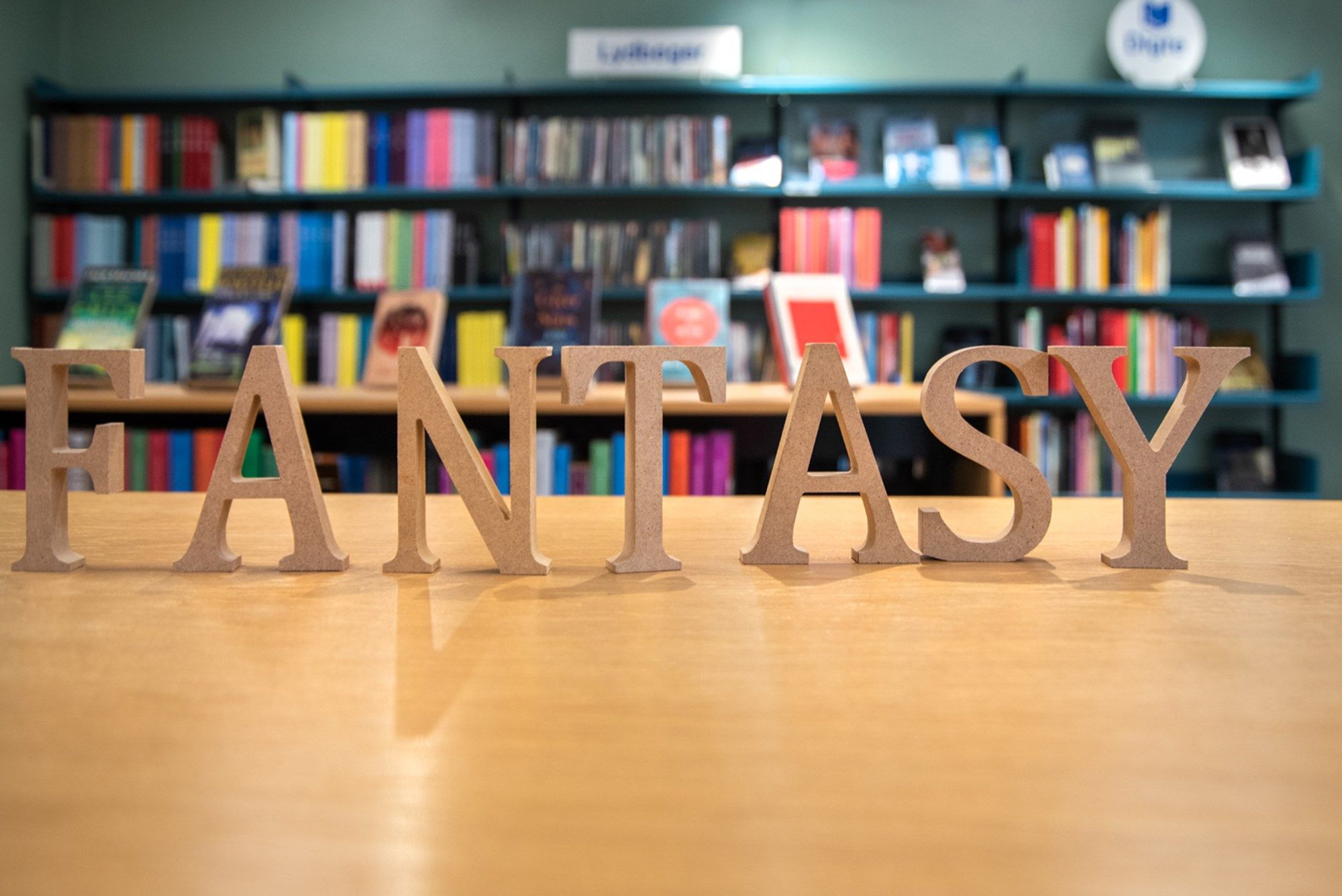 Wooden letters spelling "FANTASY" on a table with blurred bookshelves in the background.