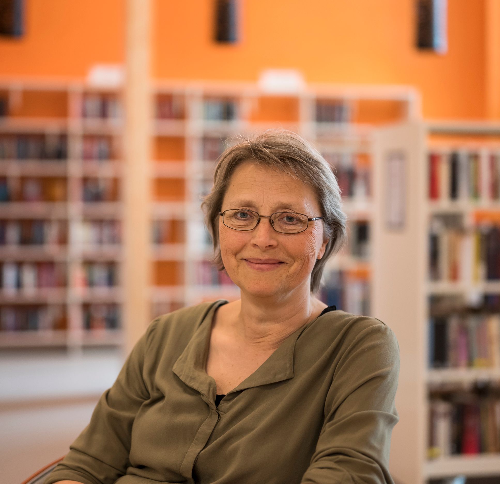 en kvinne med briller sitter ved et bord på et bibliotek