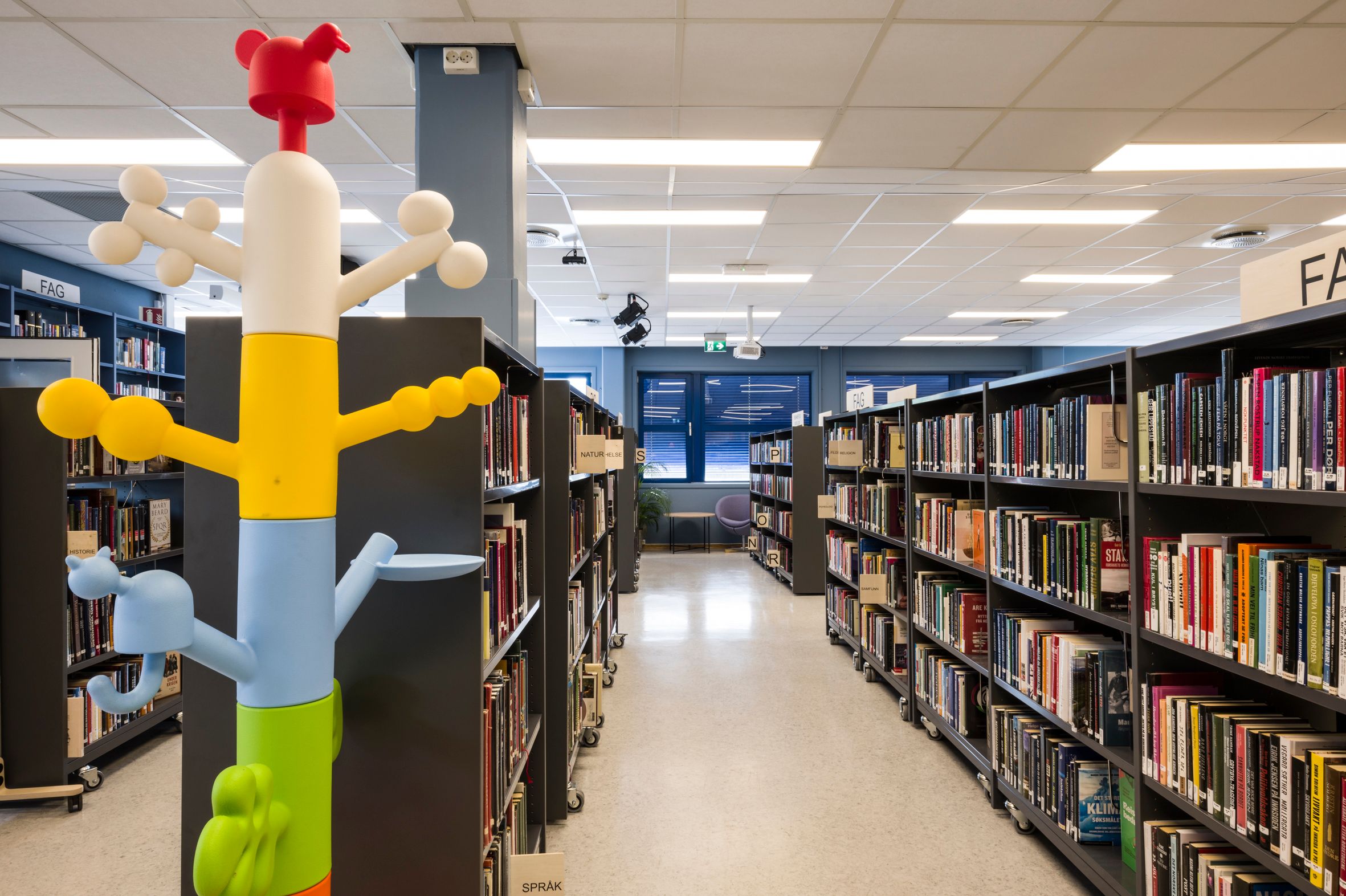 et bibliotek med mange bokreoler og en fargerik stumtjener