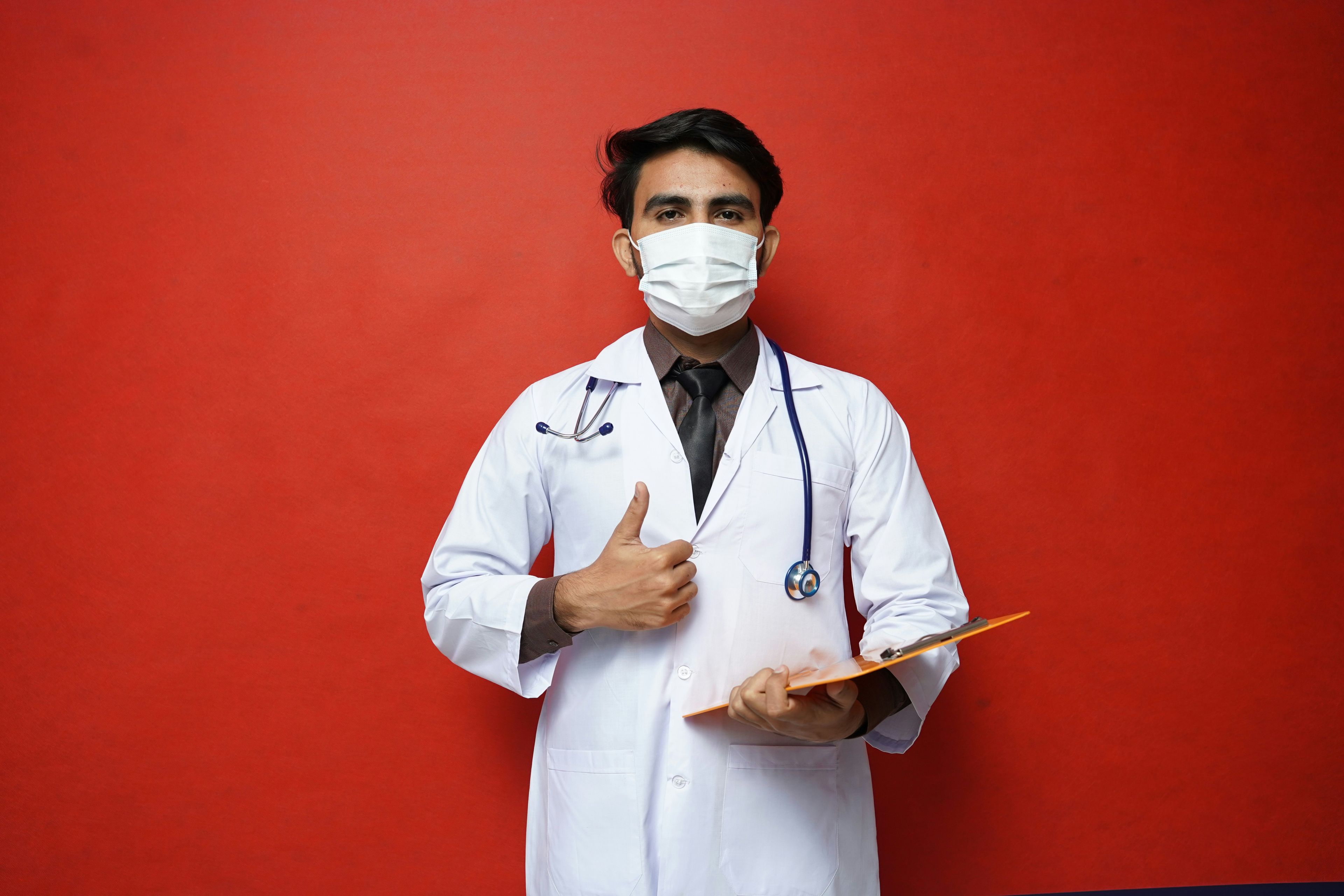 a doctor wearing a mask and holding a clipboard is giving a thumbs up .