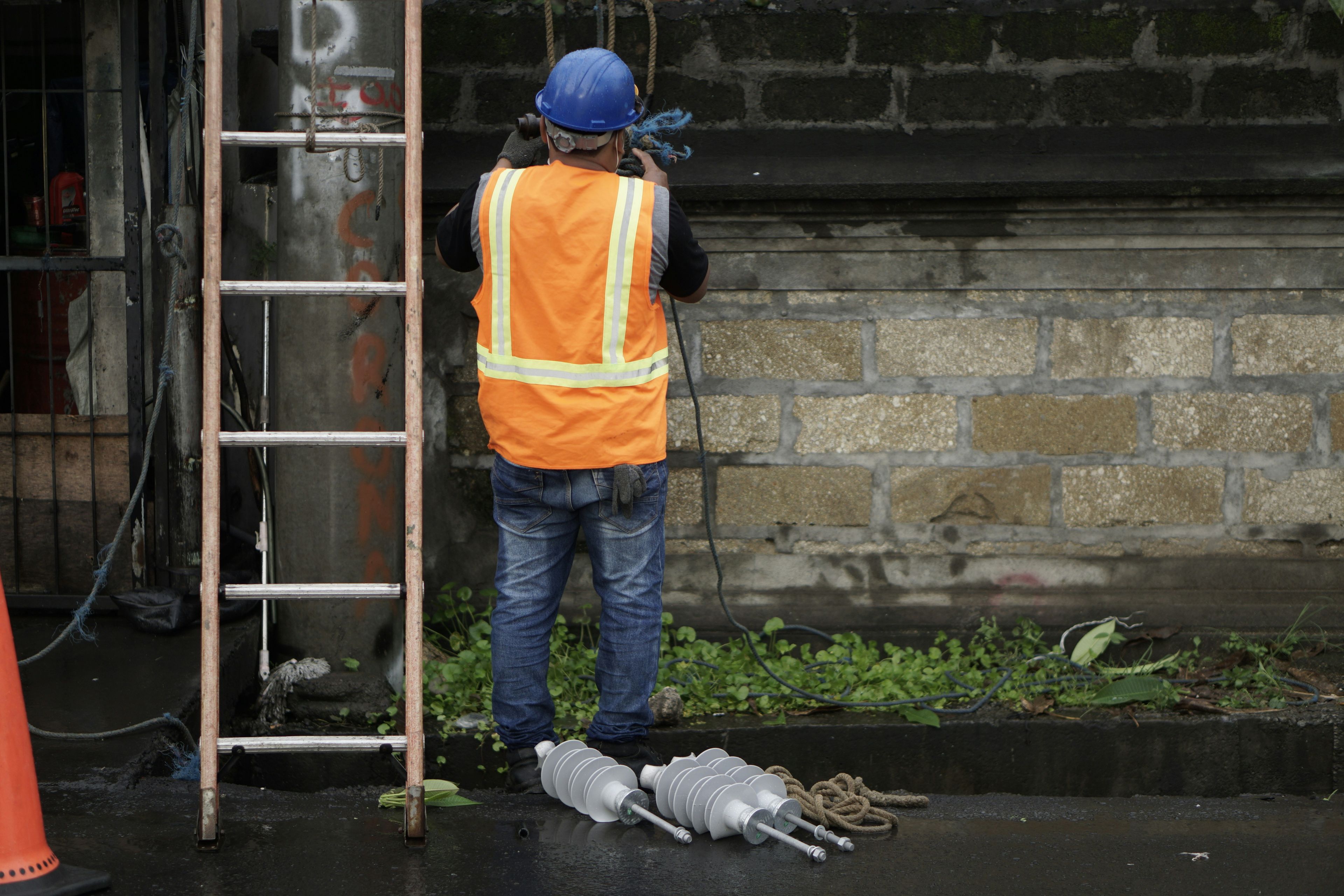 a man in an orange vest and hard hat is standing next to a ladder .