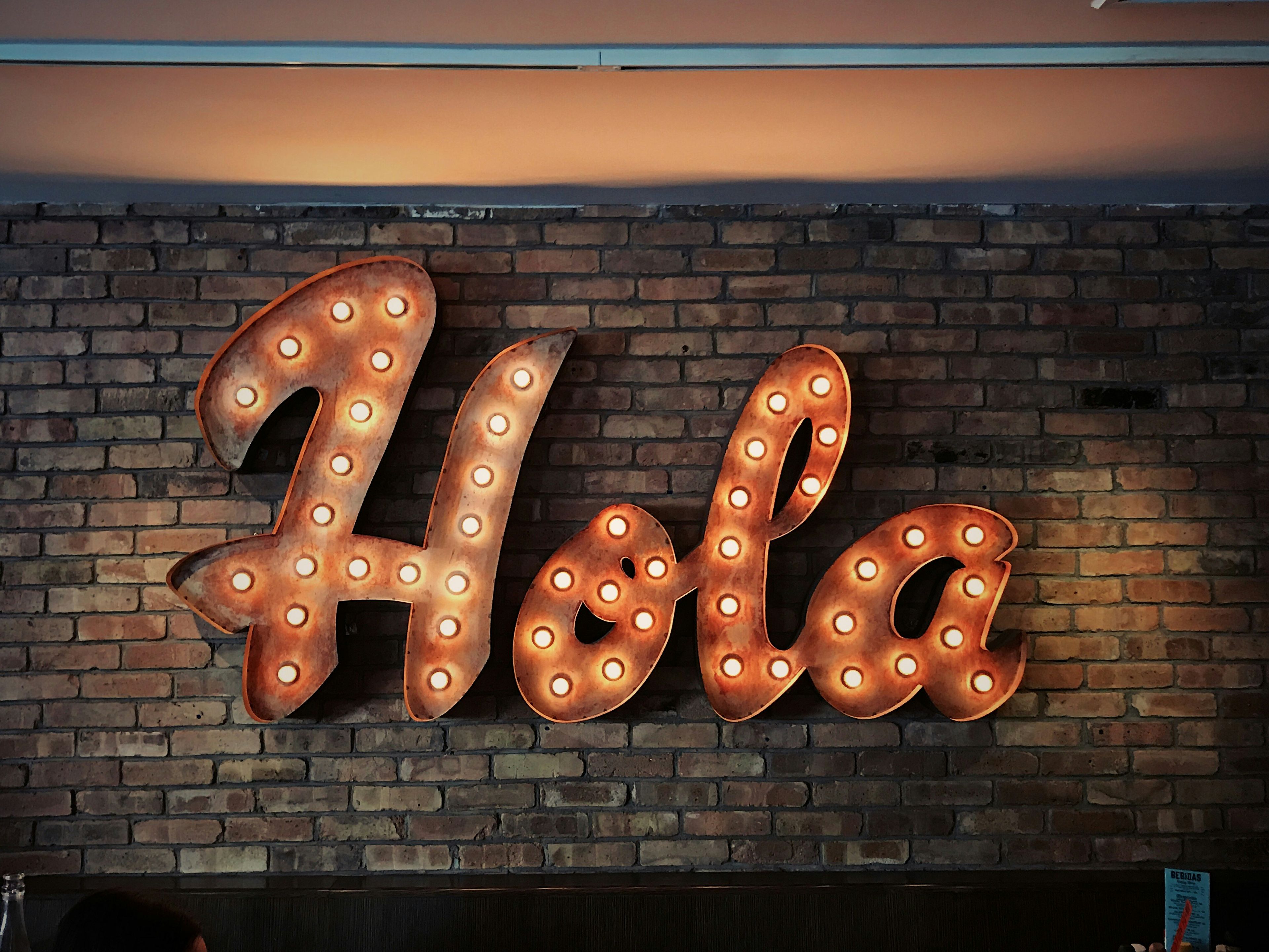 a lighted sign that says hola on a brick wall .