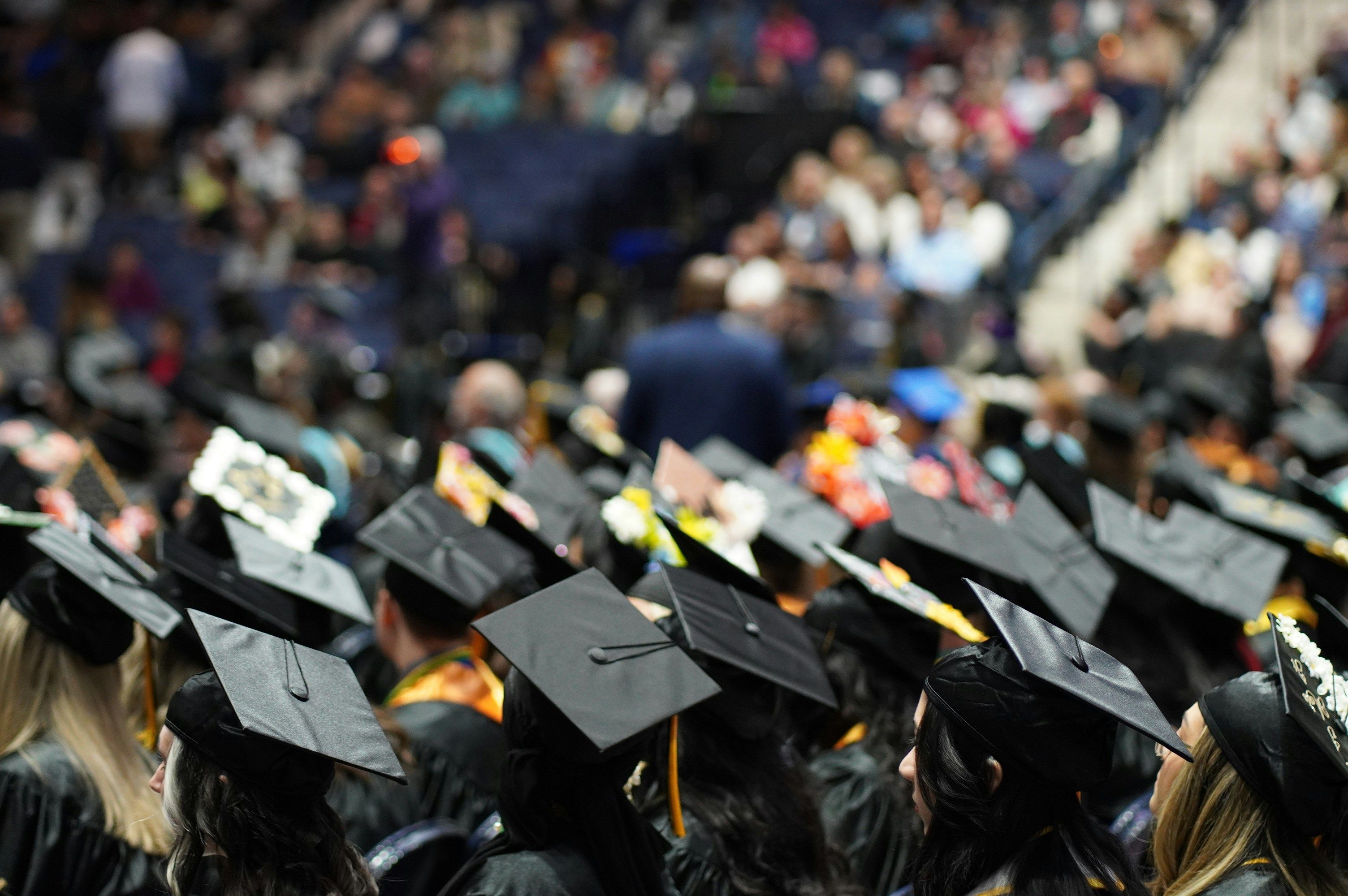 a crowd of graduates are sitting in a stadium wearing graduation caps and gowns .