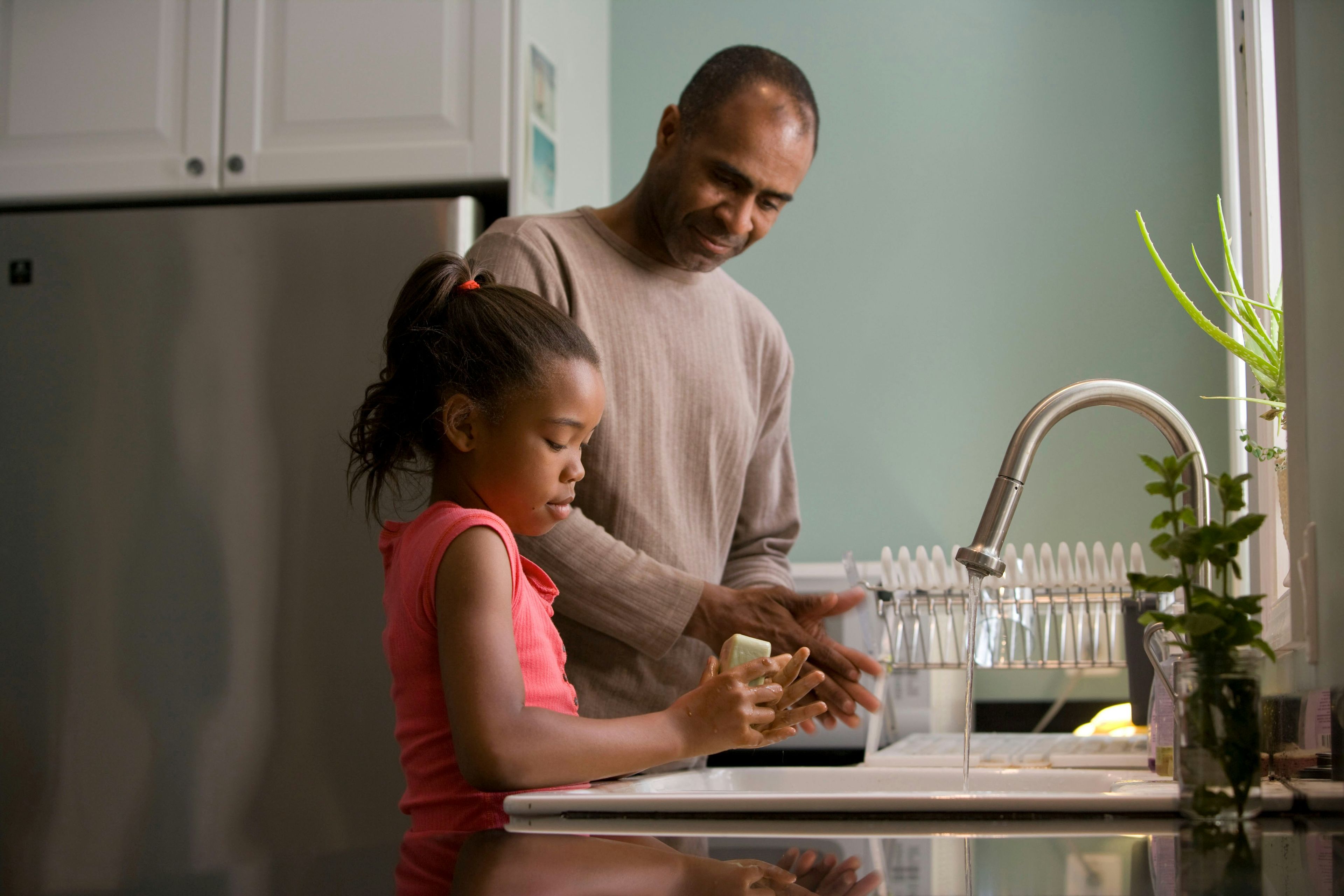a man and a little girl are washing their hands in a kitchen sink .