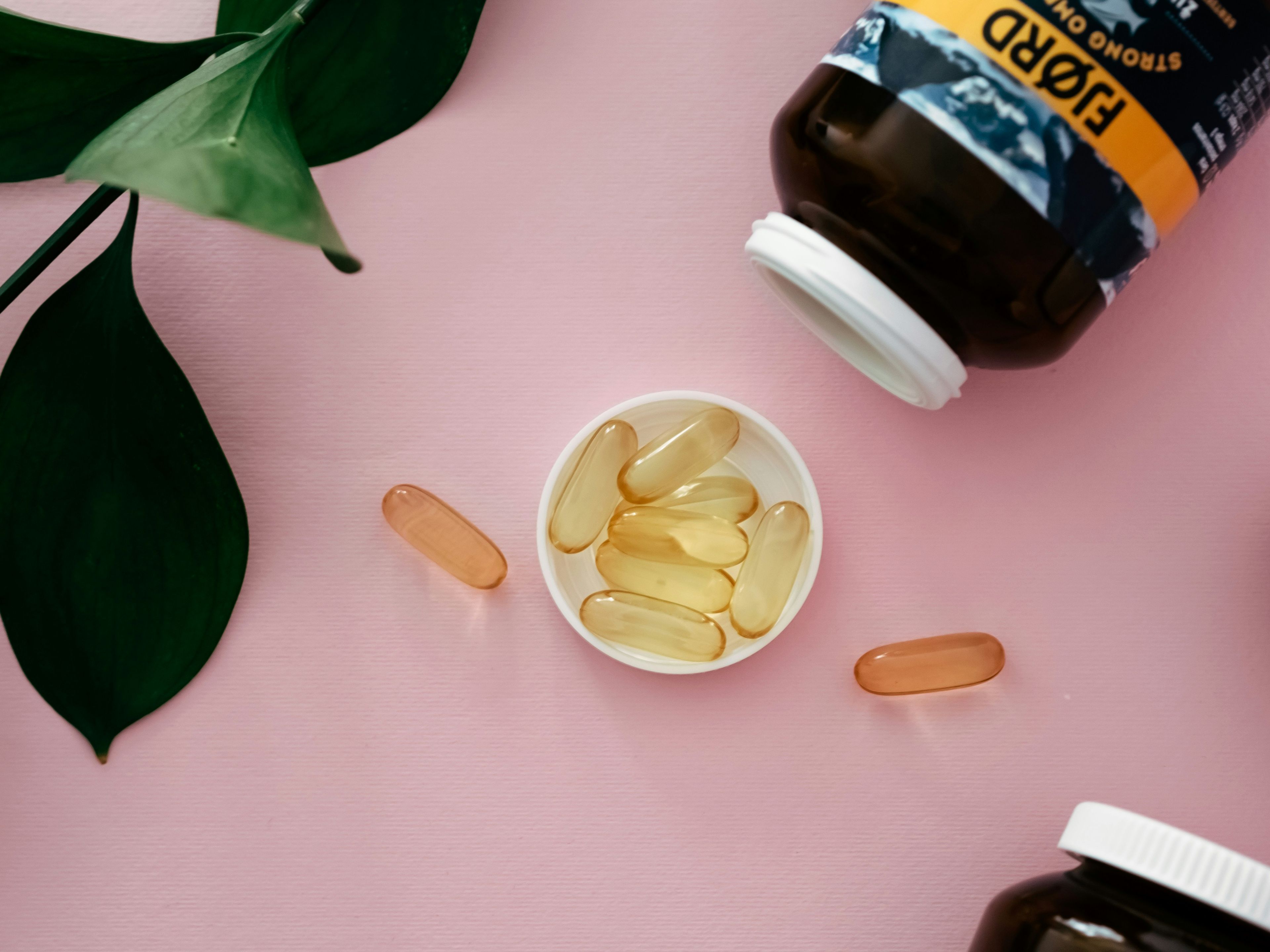 a bowl of fish oil capsules next to a bottle of fish oil on a pink surface .
