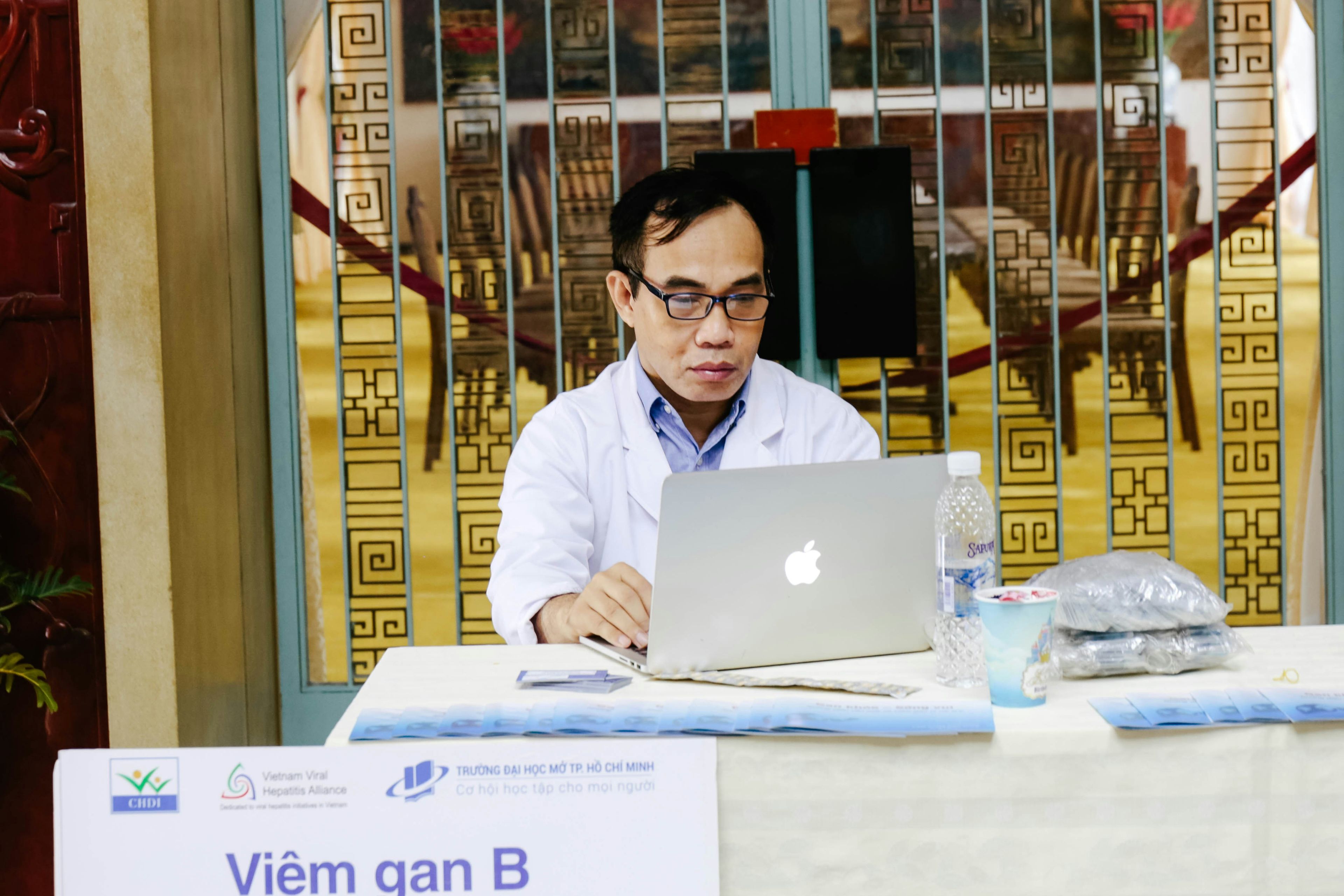 a doctor is sitting at a table using a laptop computer .