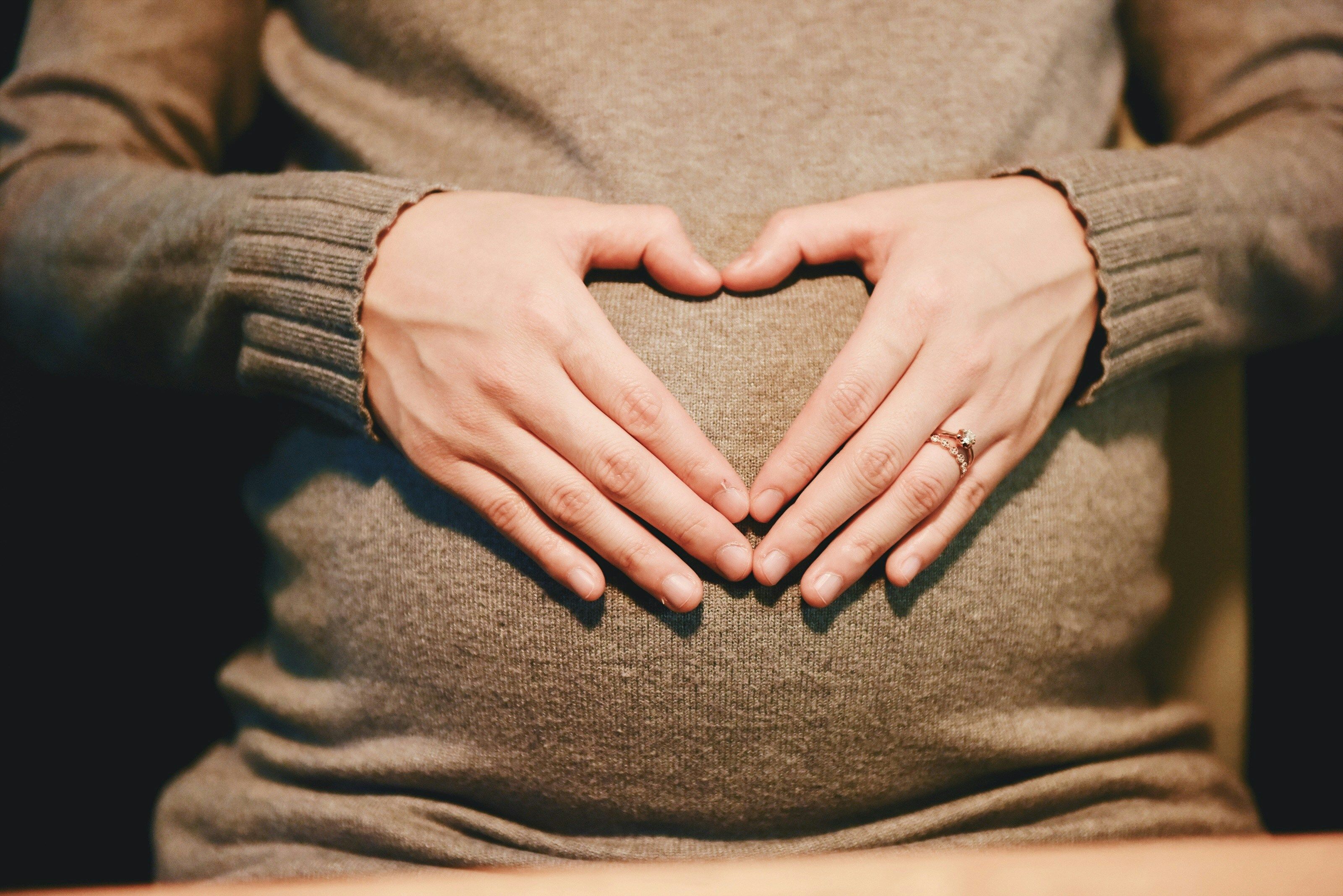 a pregnant woman is making a heart shape with her hands on her belly .