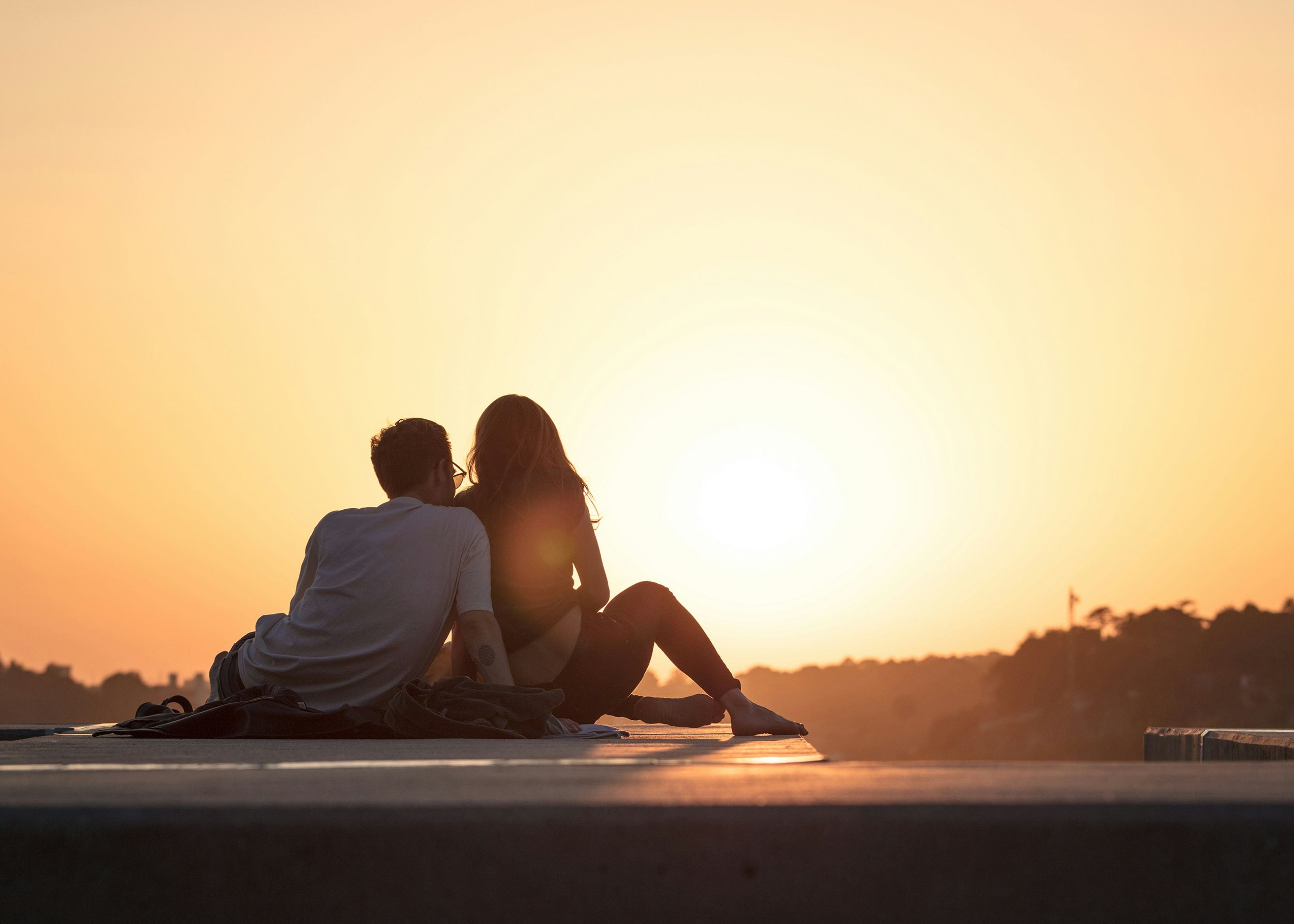 a man and a woman are sitting on the ground watching the sunset .