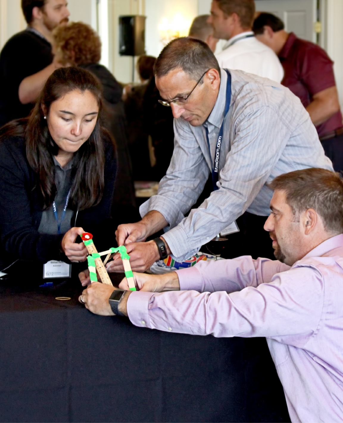 Three participants building a catapult from craft sticks and rubber bands at a workshop table