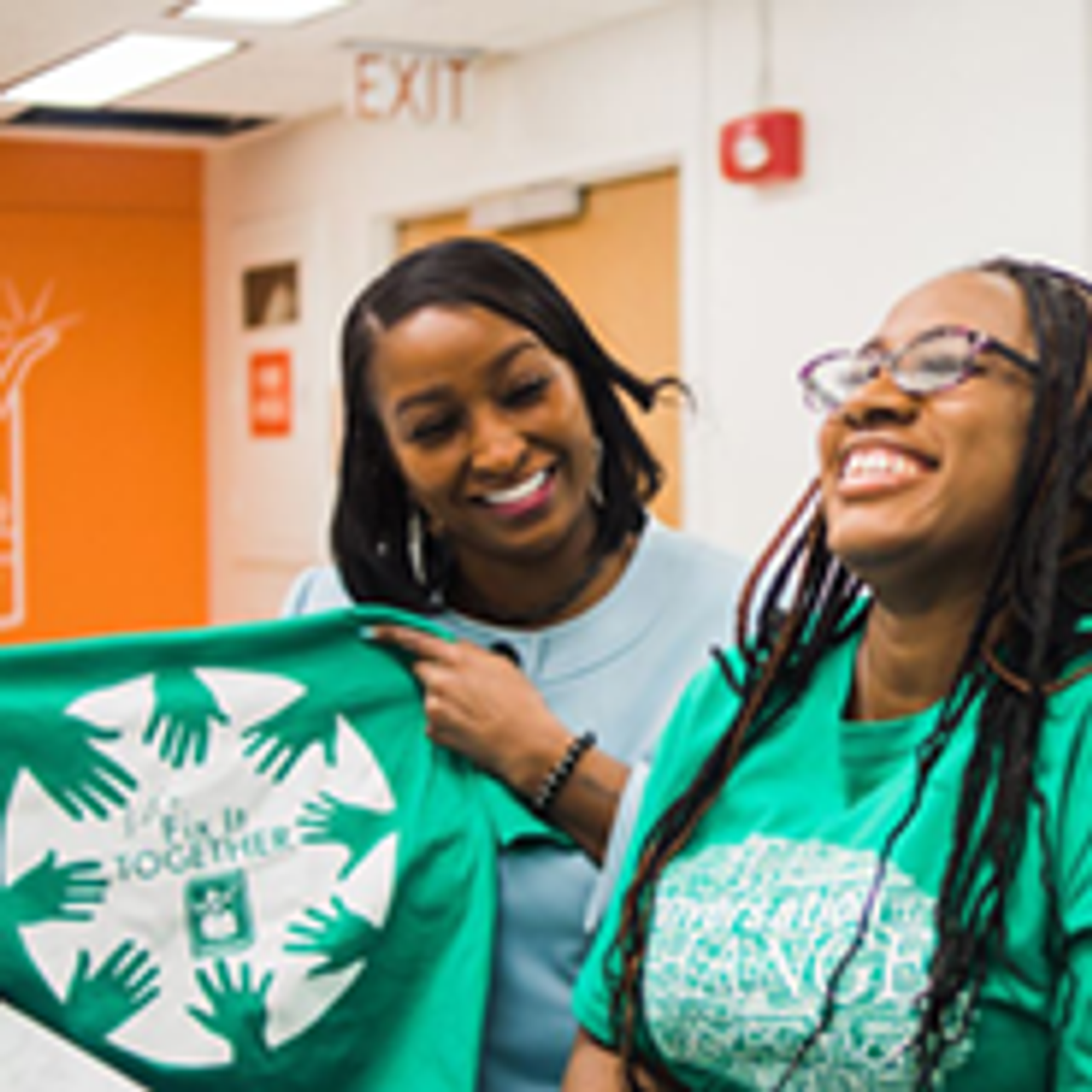 Two women smiling while holding up a t-shirt saying 'Fix it together'