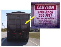 A dump truck with a  small sign in the lower right corner of the back of the truck that reads Caution stay back 200 feet