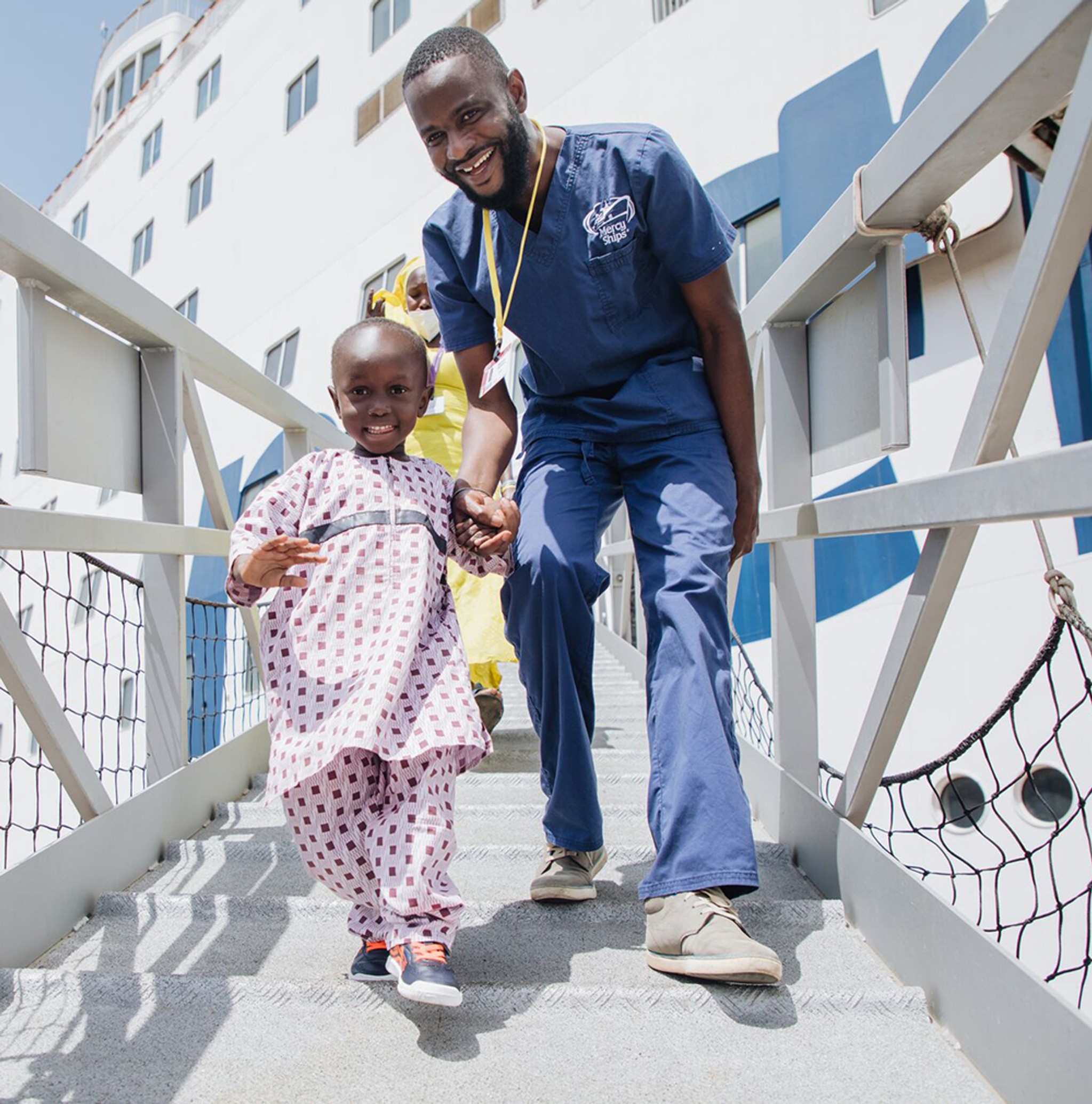 Medical professional helping small child down a walkway from a hospital ship