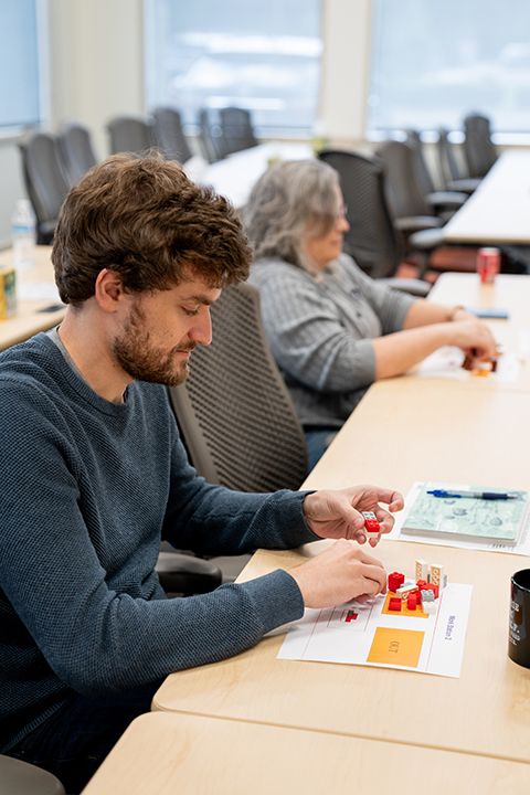 Two participants assembling LEGO pieces at a long table using printed work instructions