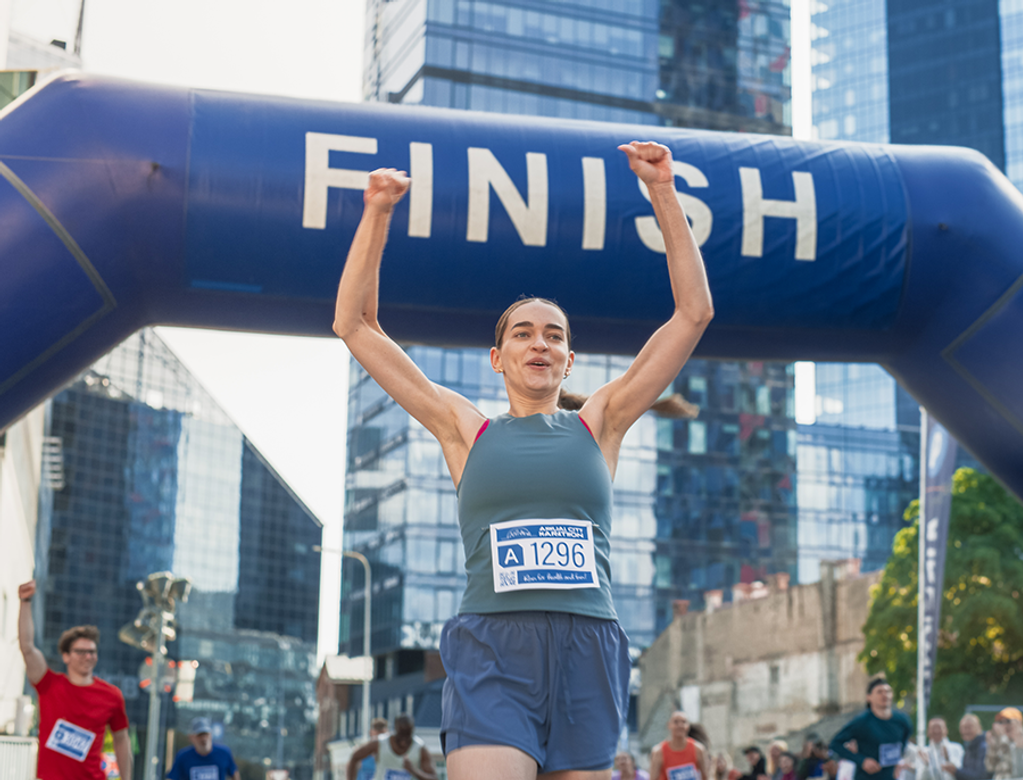 woman with raised arms in happiness as she crosses the finish line, winning a marathon race.
