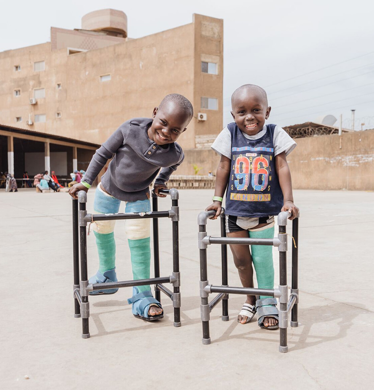 Two happy children with casts and walkers outside a concrete industrial complex