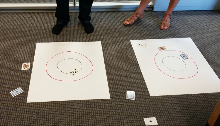 Two paper floor targets with playing cards scattered around them showing where each card landed